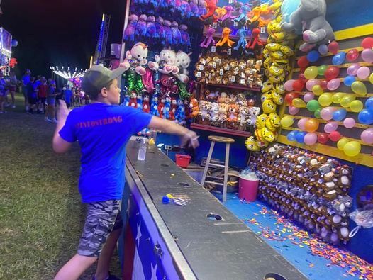 Man throwing a ball at a colorful carnival balloon-shooting booth at night