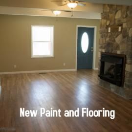A room with neutral beige walls, wood-look flooring, a stone fireplace, and a blue door with an oval glass insert.
