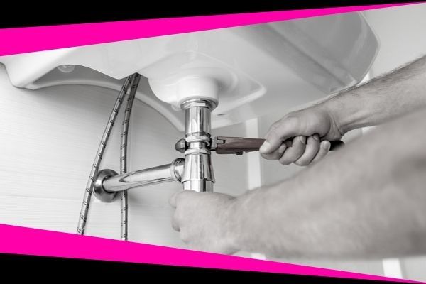 A close-up of a person using a wrench to repair the metal P-trap pipe under a bathroom sink.