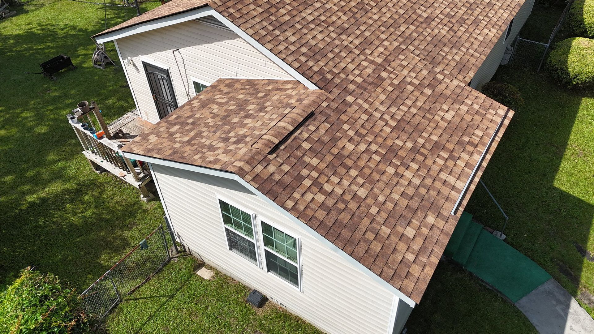 Aerial view of a house with a brown shingle roof, light-colored siding, and green grass.