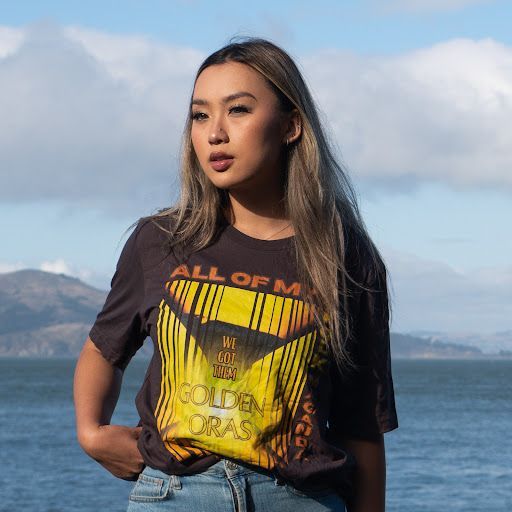 A woman wearing a black and yellow t-shirt is standing in front of a body of water.