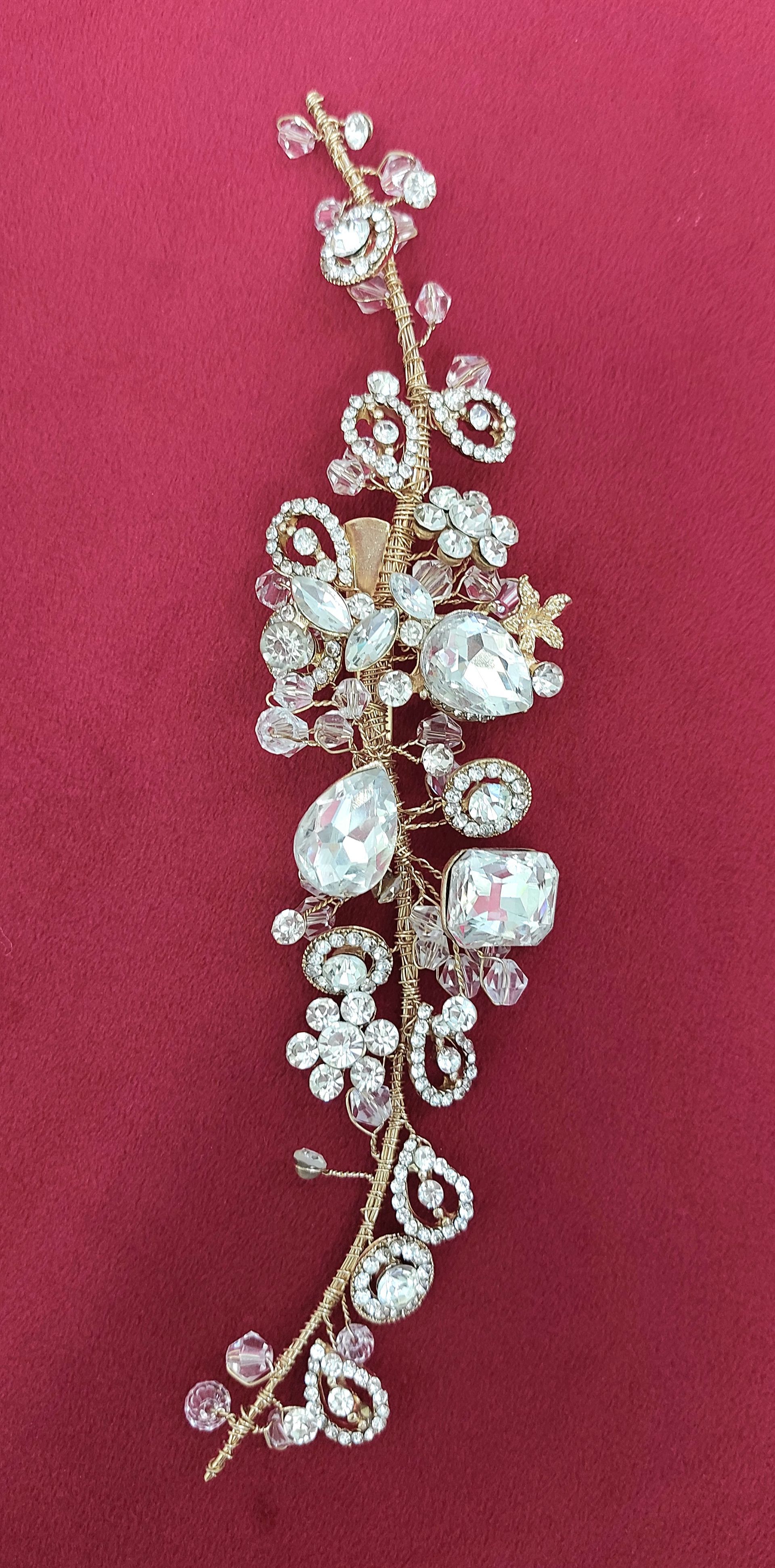 Parrucca per capelli decorata con gioielli dorati e cristalli trasparenti su sfondo rosso.