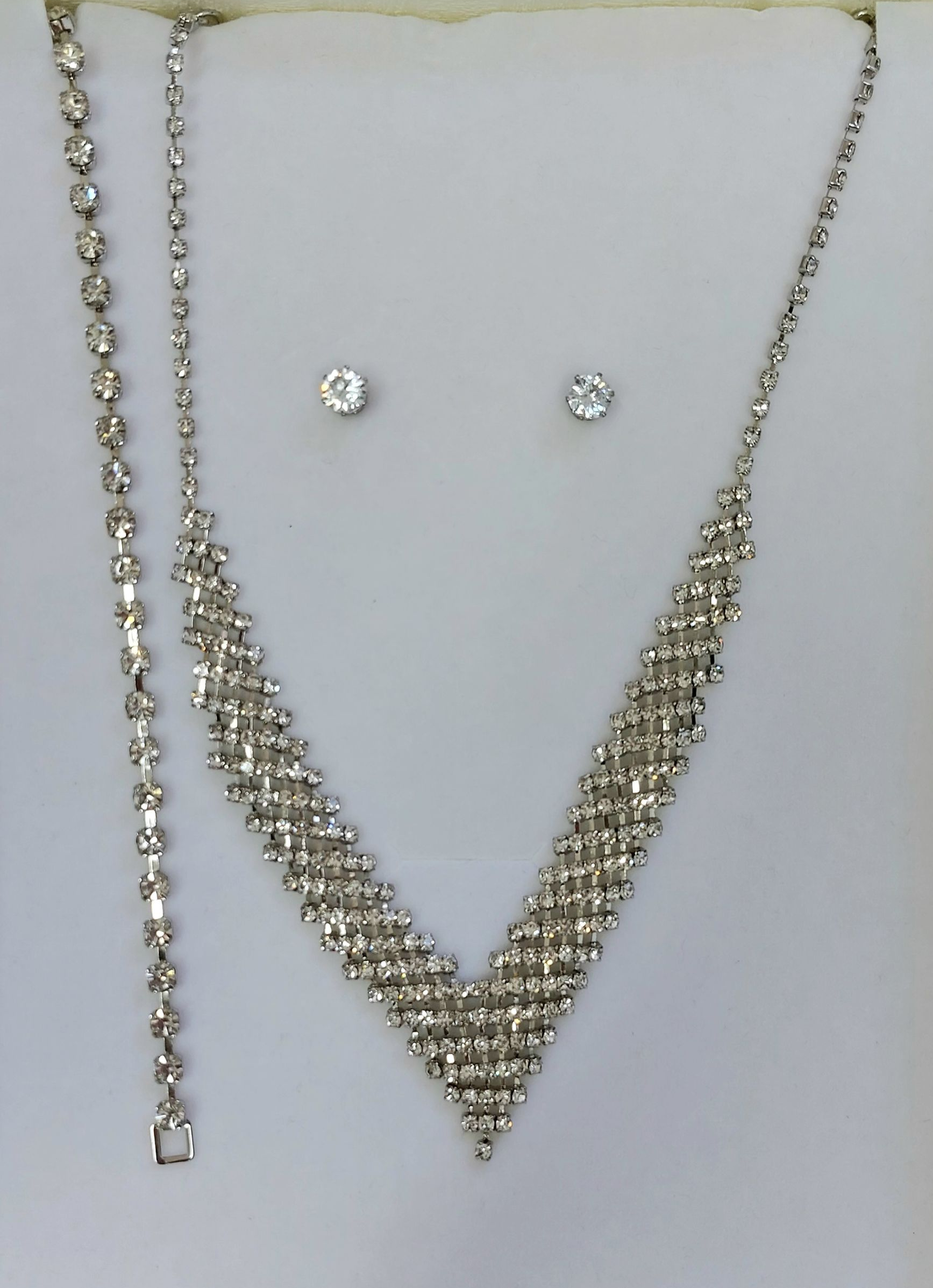 Set di gioielli in argento: collana, bracciale e orecchini con strass trasparenti su sfondo bianco.