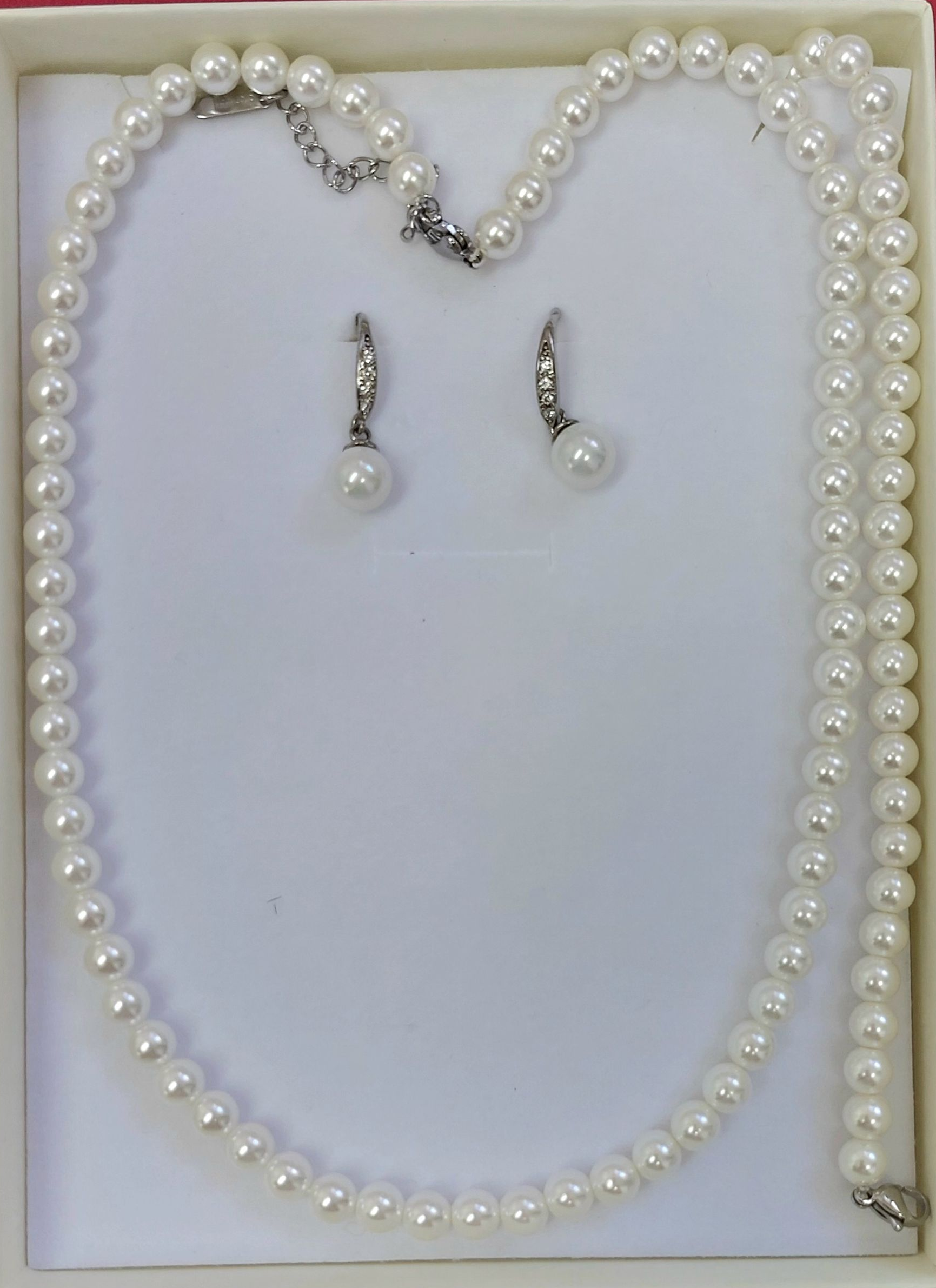 Collana di perle e orecchini incastonati in un portagioie bianco.