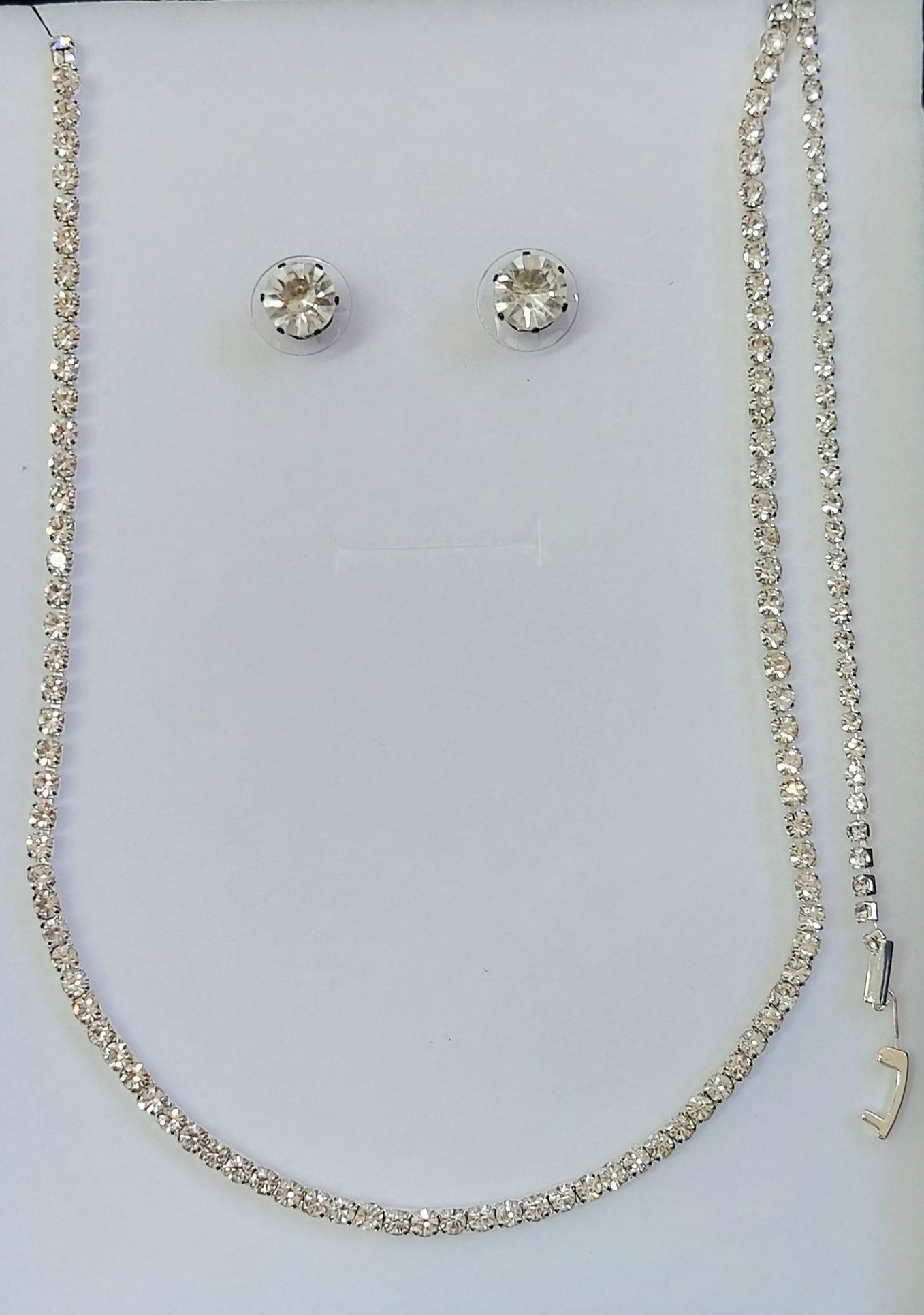 Collana di diamanti e orecchini a bottone su sfondo bianco.