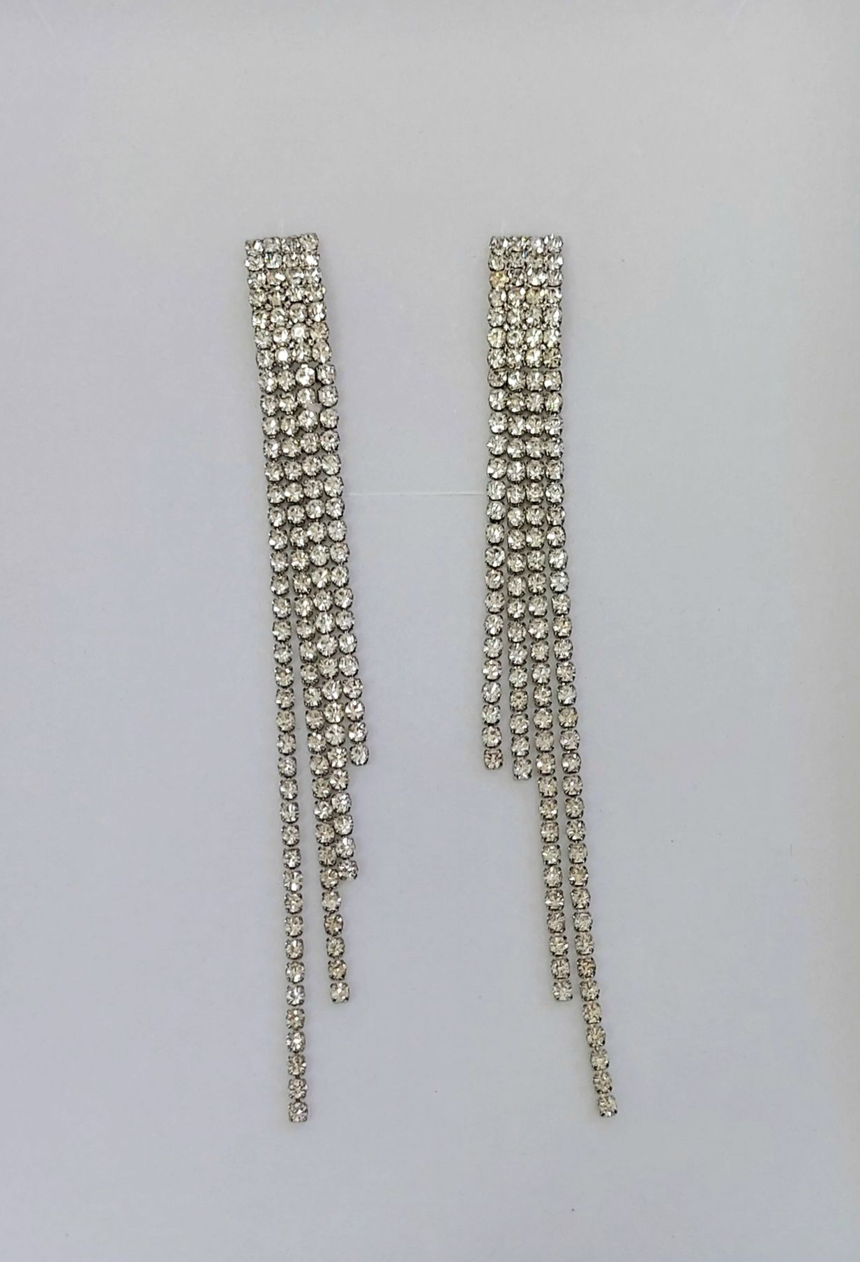 Orecchini con nappe in strass argentati su sfondo bianco.