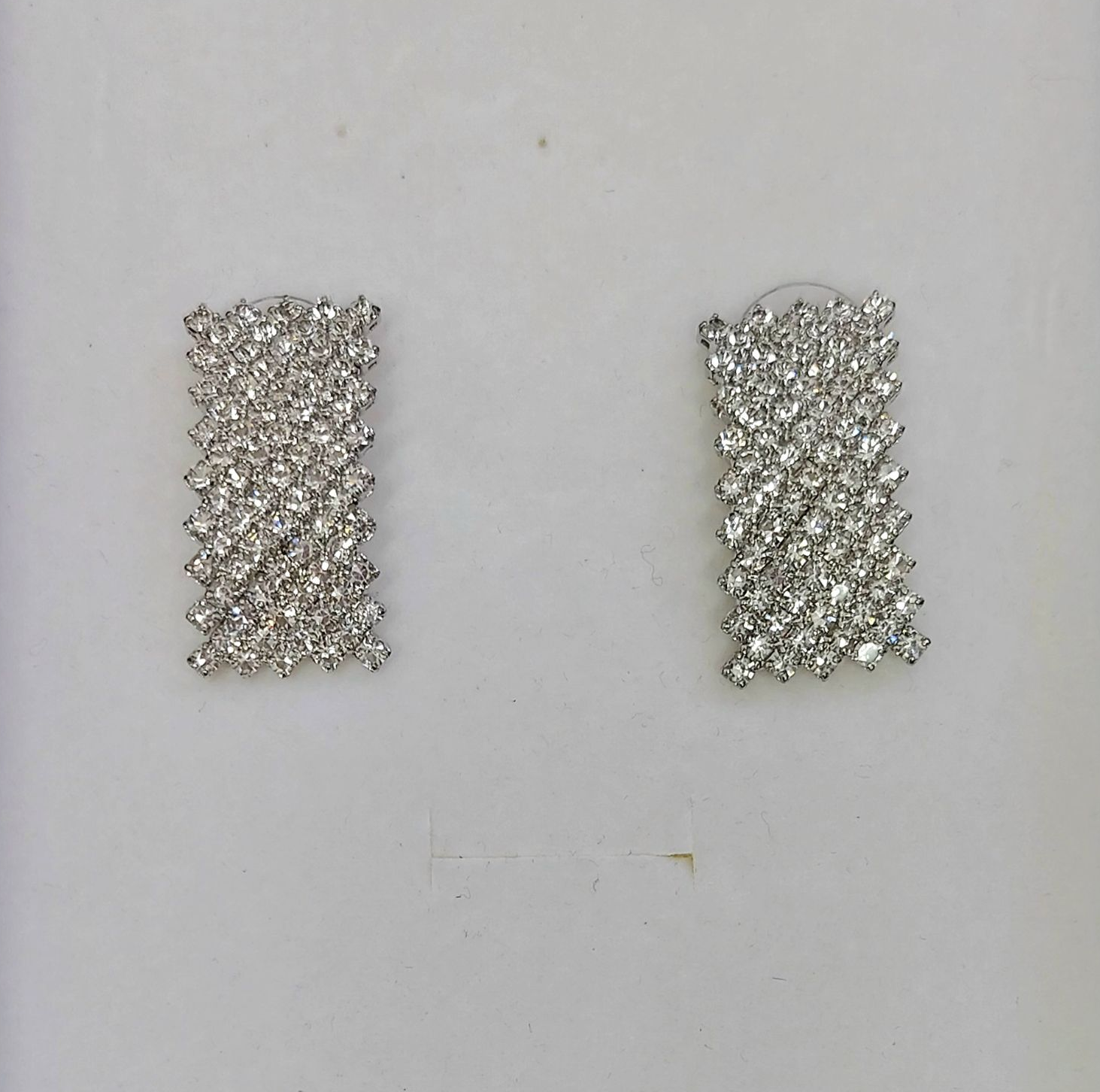 Orecchini rettangolari in argento, fittamente tempestati di cristalli trasparenti, su sfondo bianco.