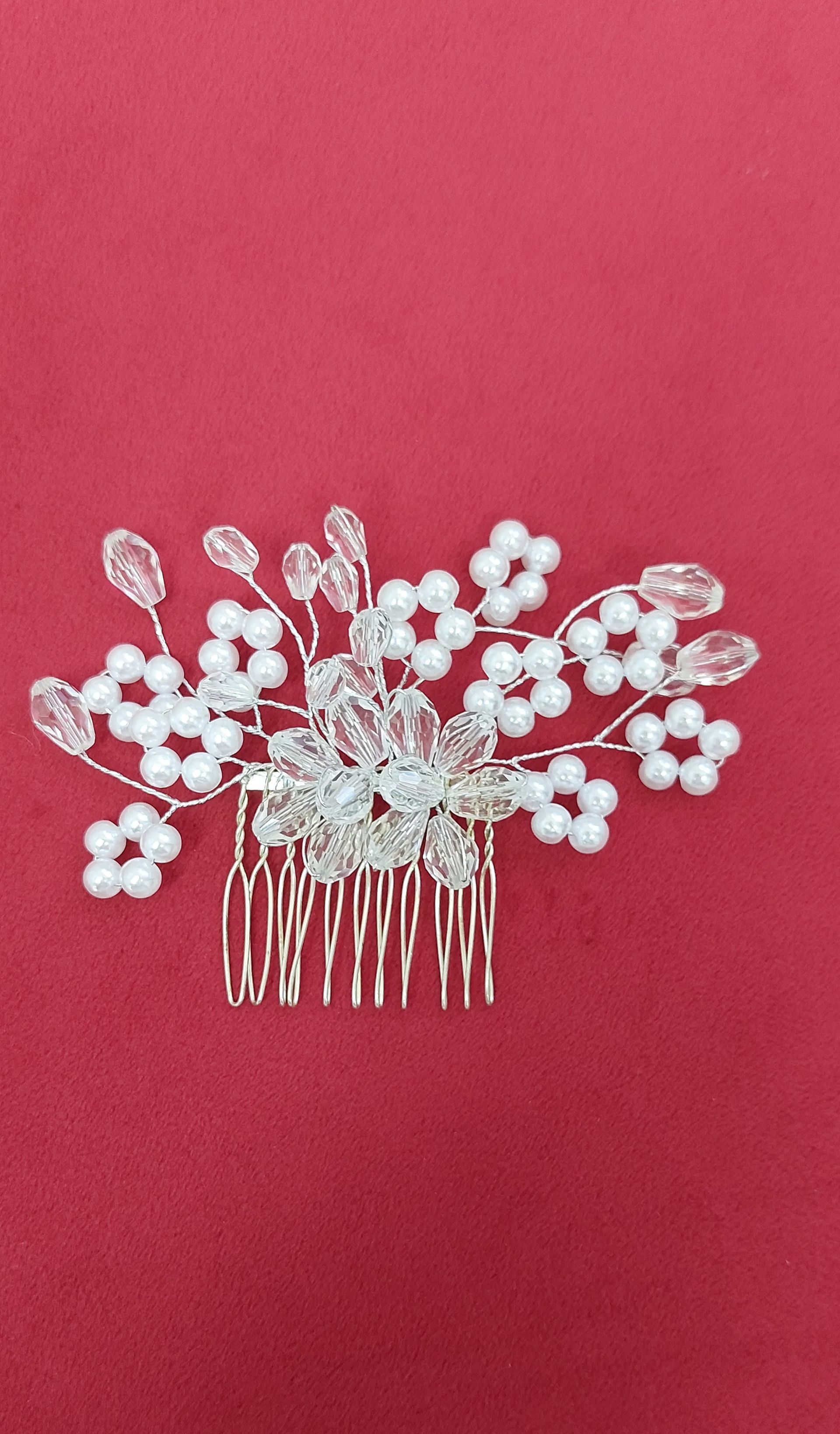 Pettine per capelli in argento con perle bianche e cristalli su sfondo rosso.