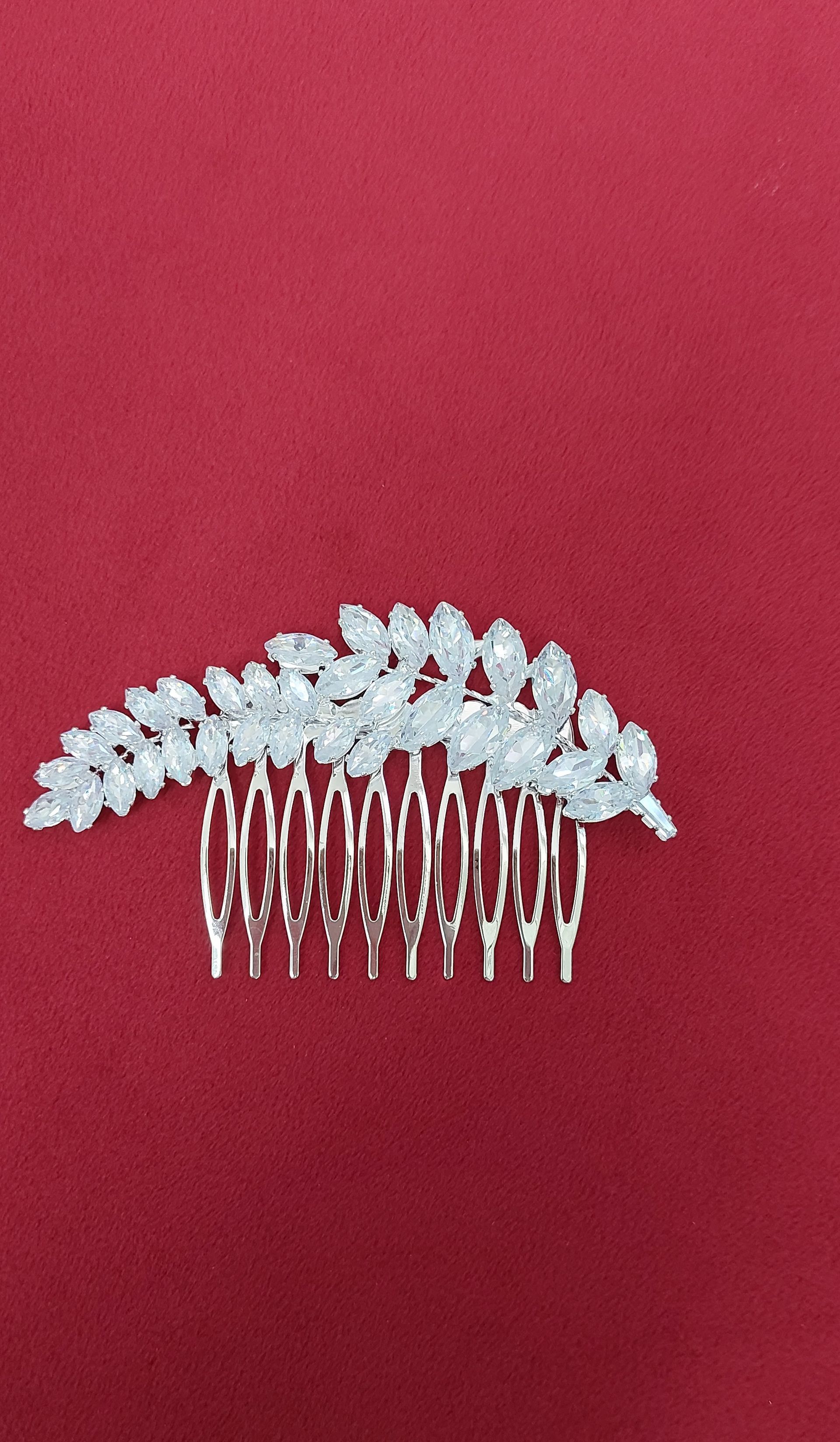Pettine per capelli in argento con cristalli trasparenti, disposti a forma di foglia, su sfondo rosso.