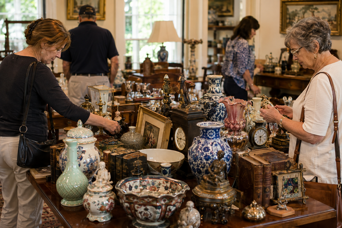 Antique shop with shoppers browsing ornate ceramic vases and wooden boxes on display tables