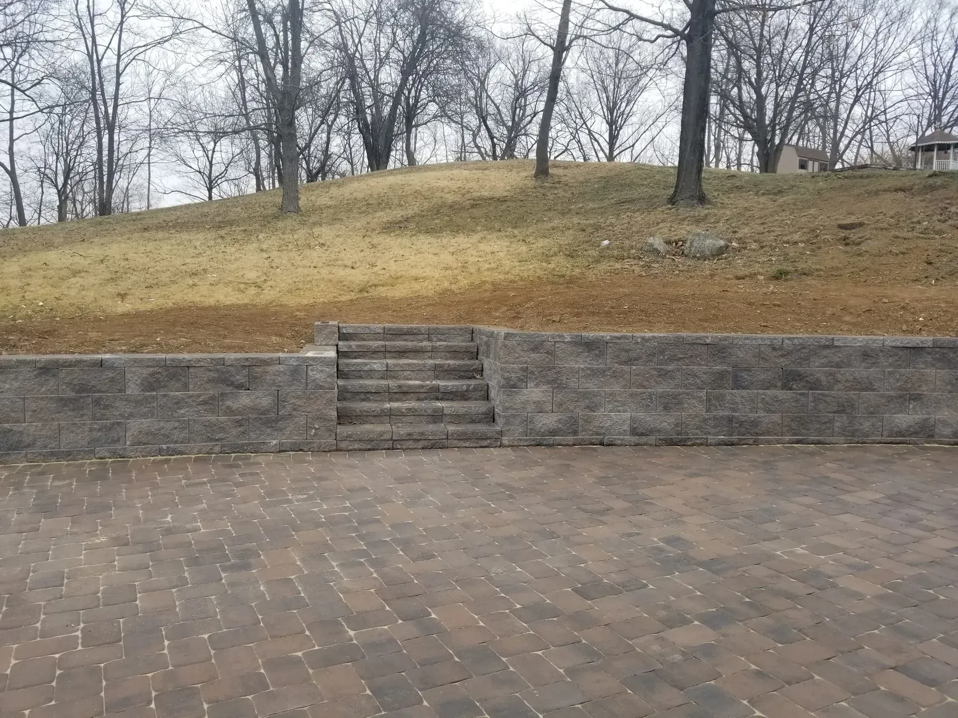 A stone wall with stairs leading up to a grassy hill.