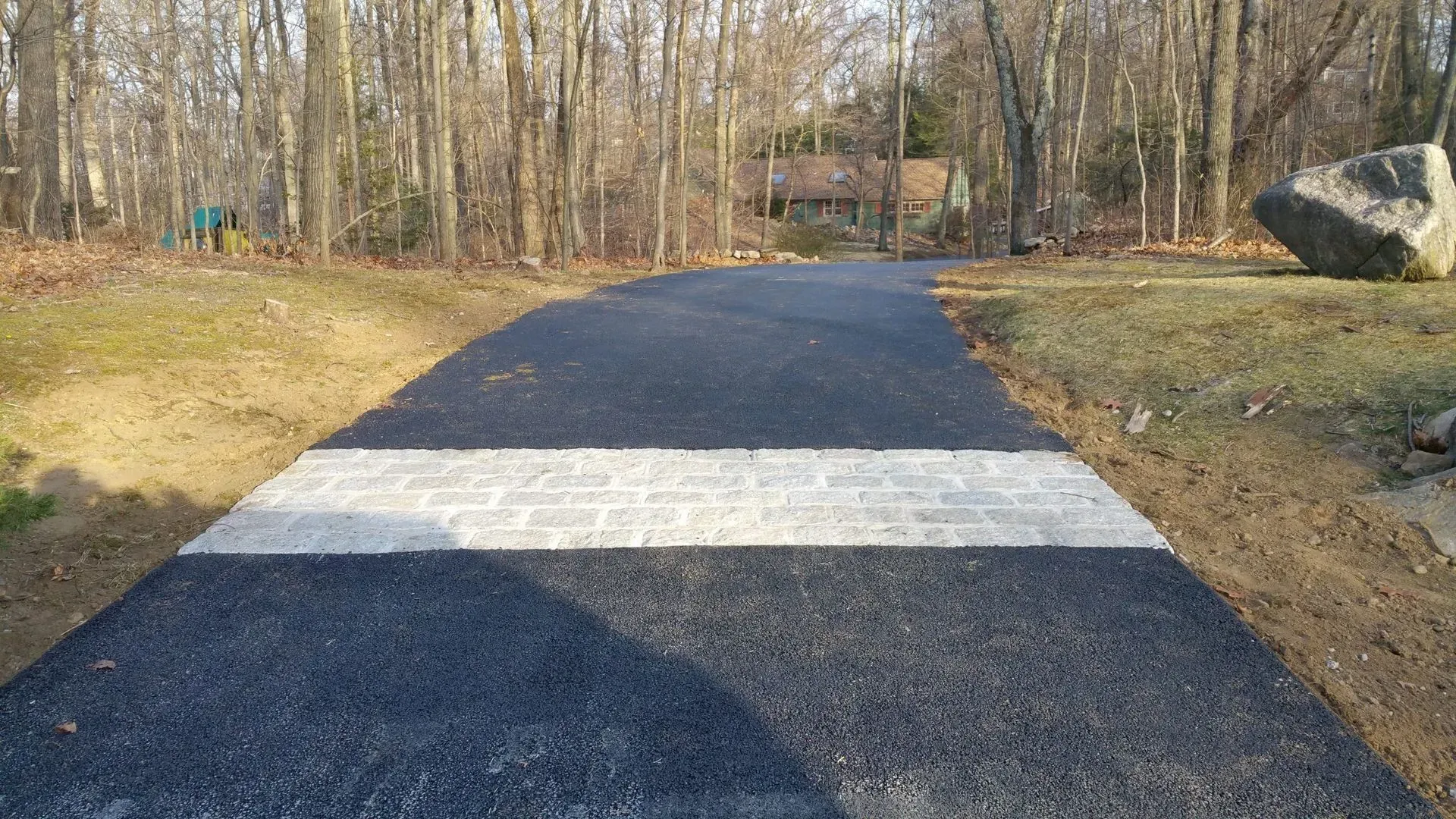 A black road with a white stripe on the side of it is going through a forest.