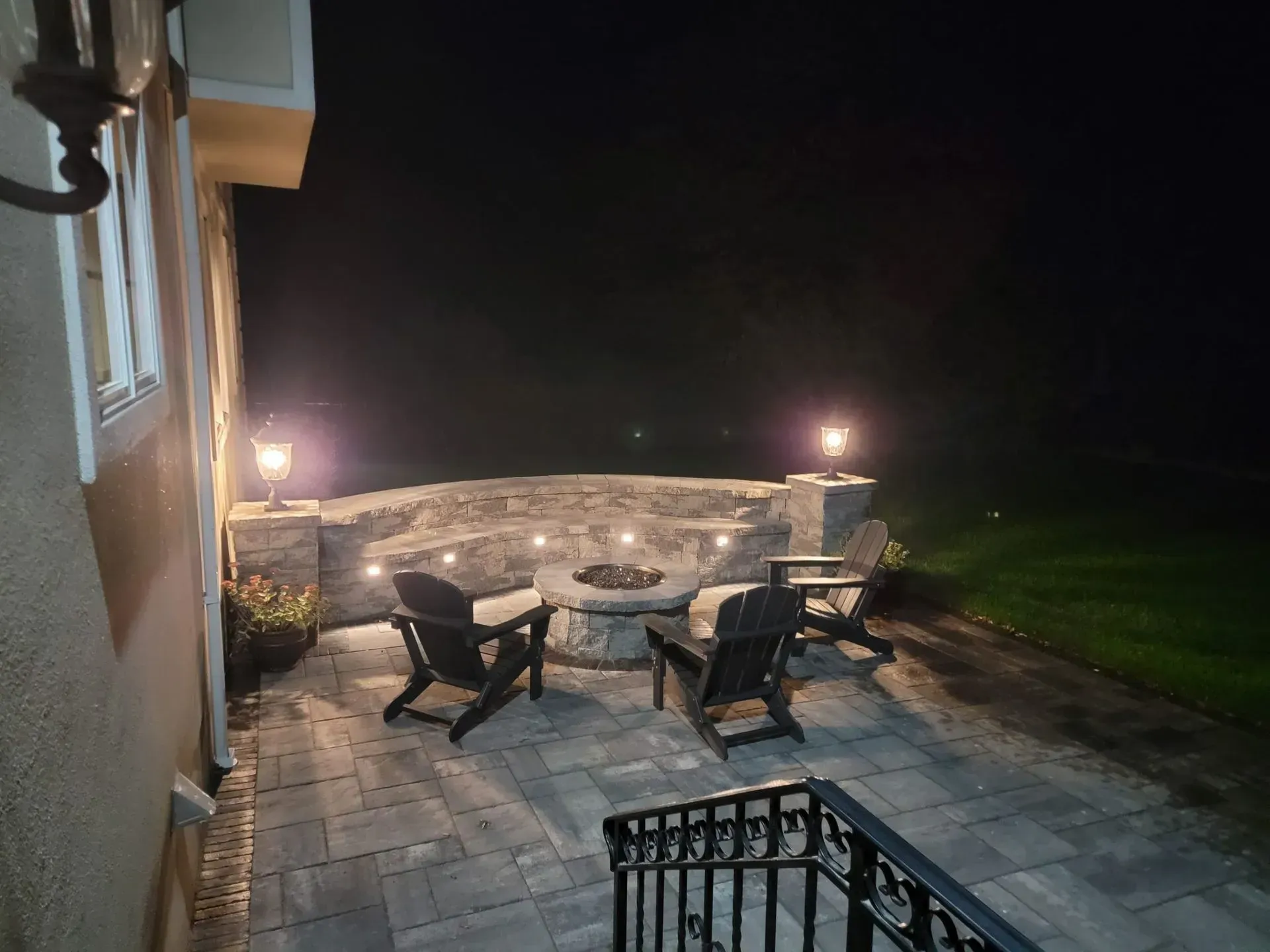 A patio with a fire pit and chairs at night.
