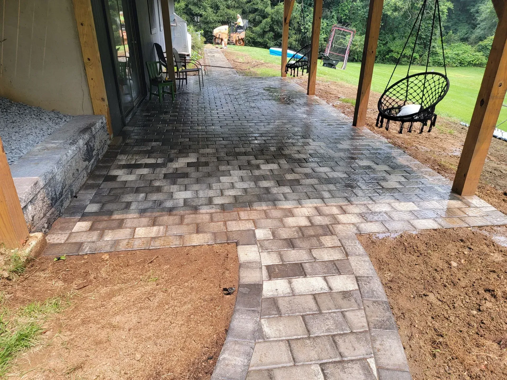 A brick walkway leading to a porch with a hanging chair.