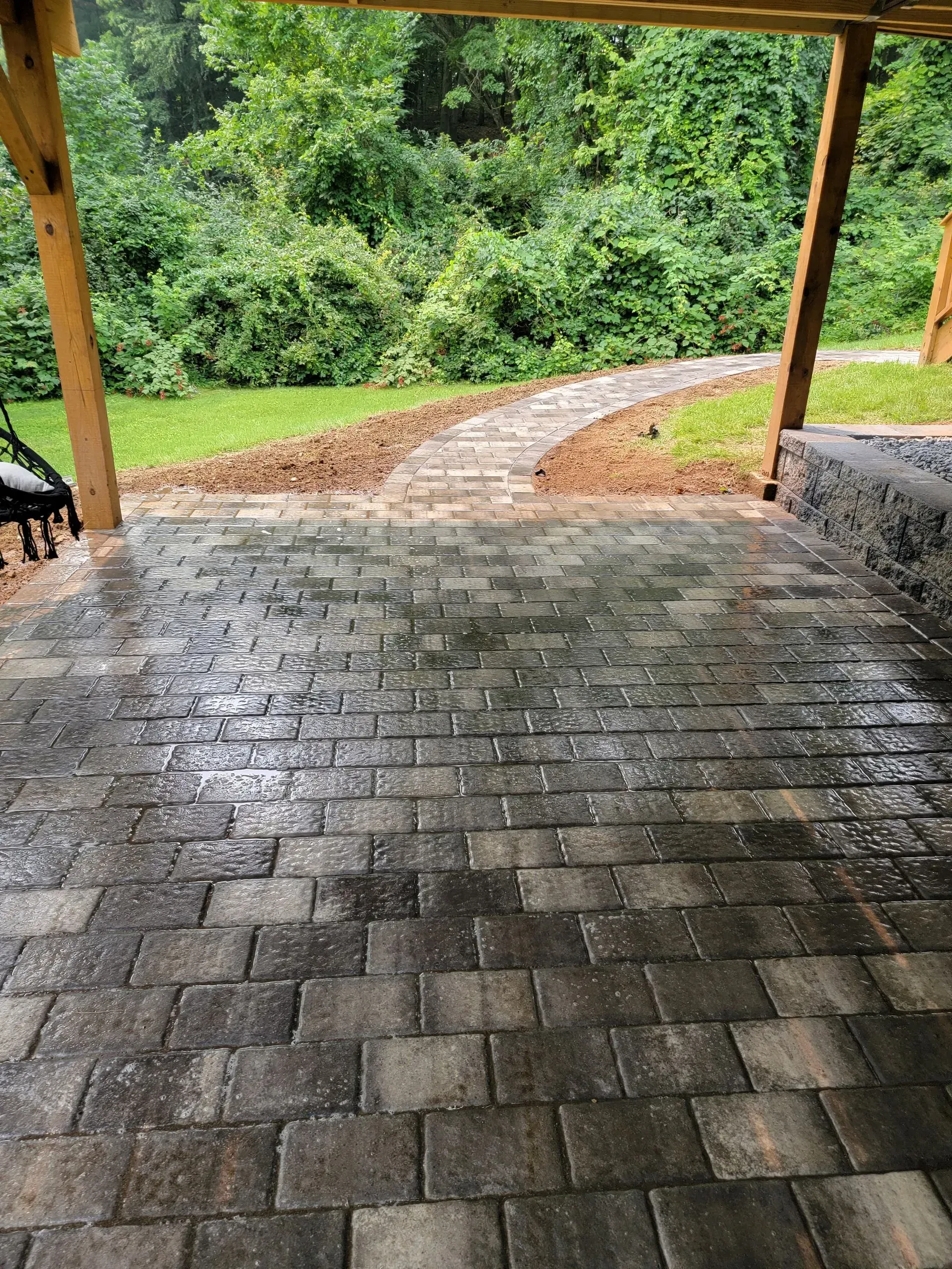 A patio with a walkway leading to a lush green forest.
