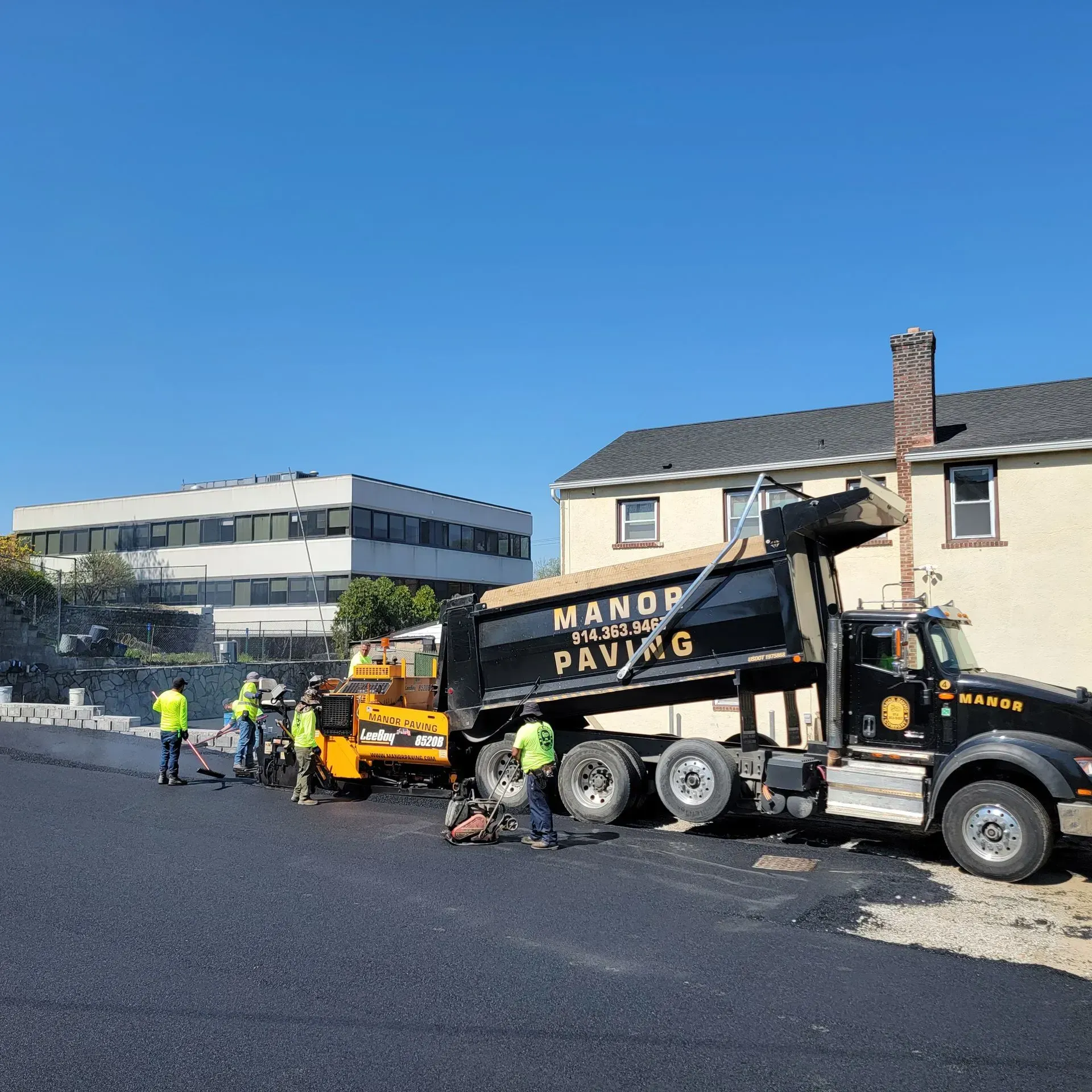 A dump truck is being loaded with asphalt in front of a building.