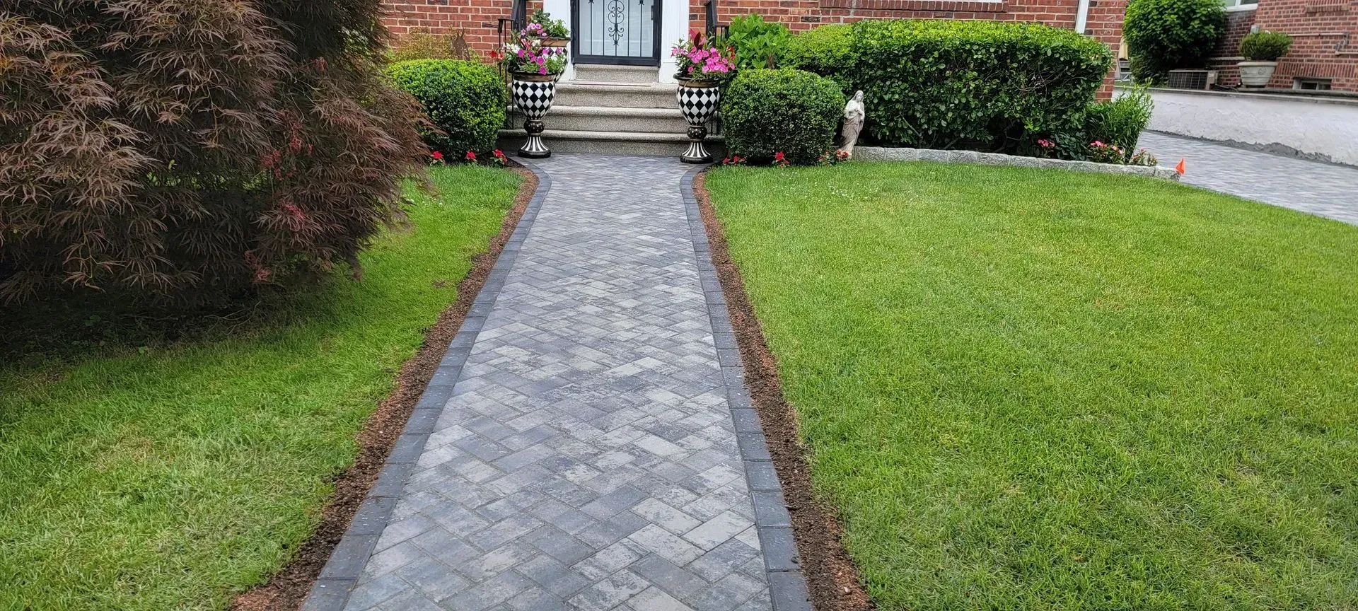 A brick walkway leading to a house with a lush green lawn.