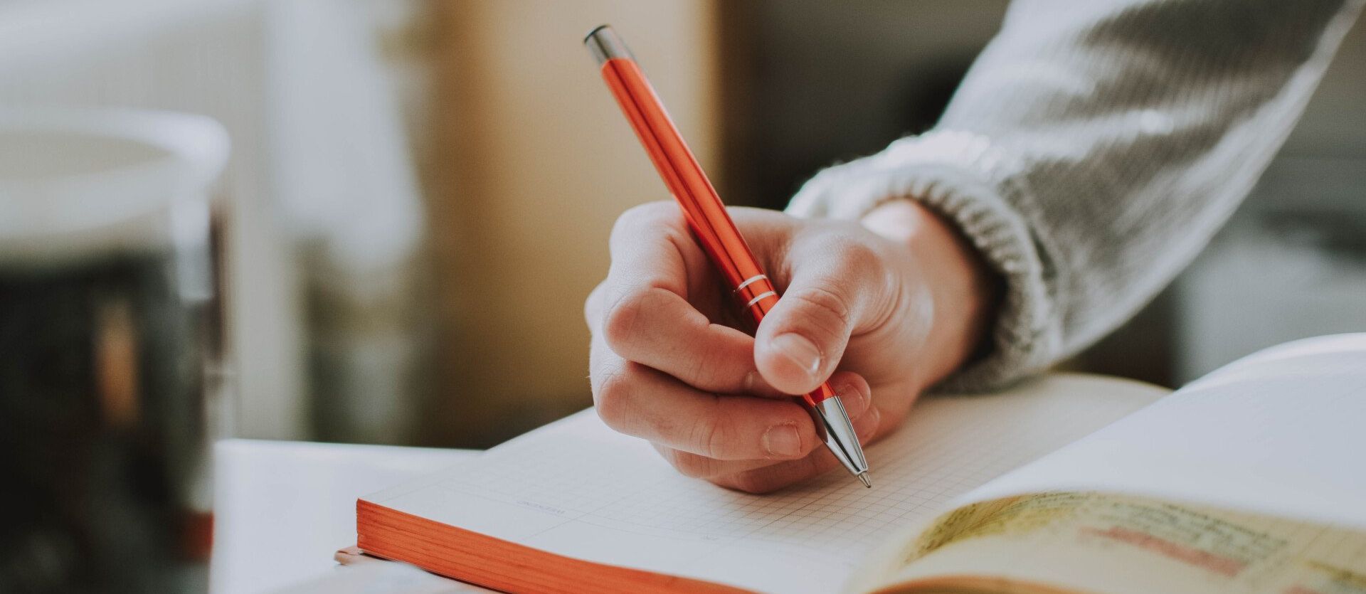 A person is writing in a notebook with a red pencil.