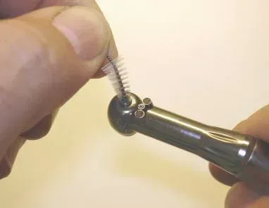 A person is cleaning a dental drill with a brush.