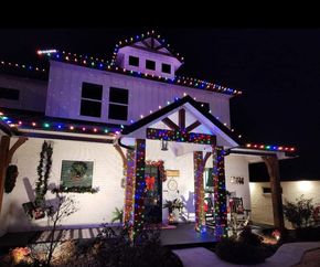 House decorated with colorful Christmas lights at night, with a lit front porch and roofline