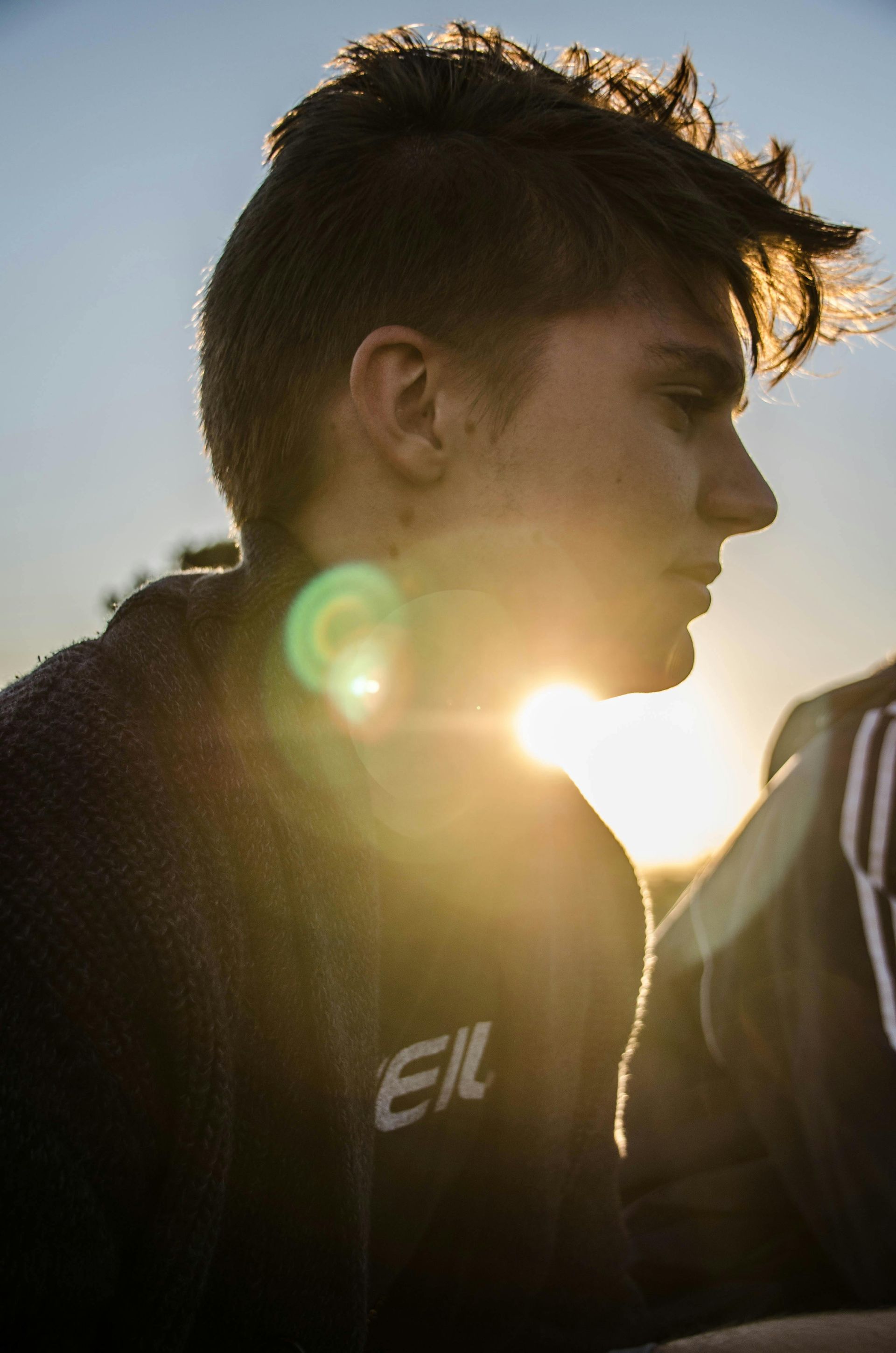 A young man with a mohawk is standing in front of a sunset.