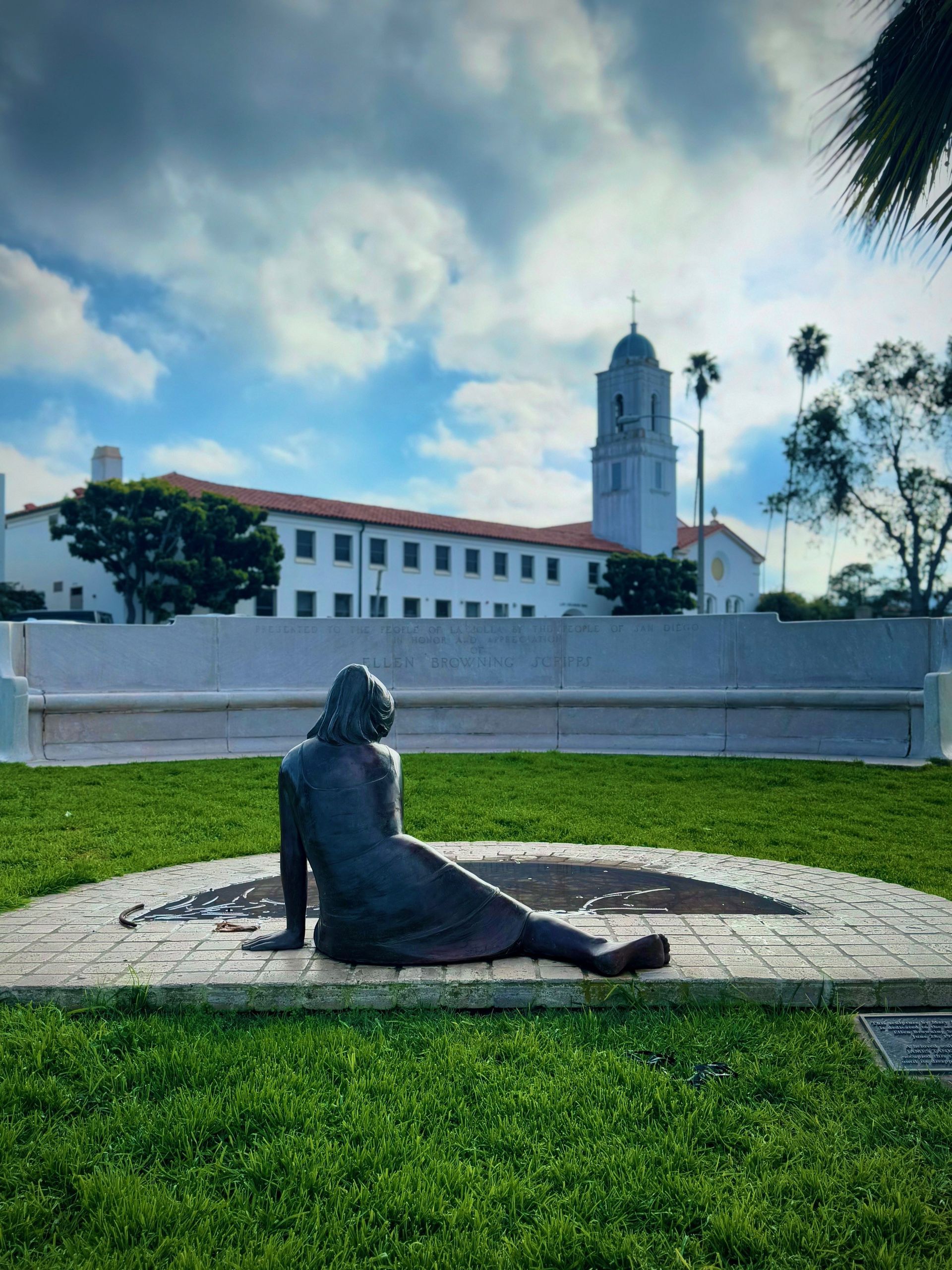 A statue of a woman is sitting in the grass in front of a building.