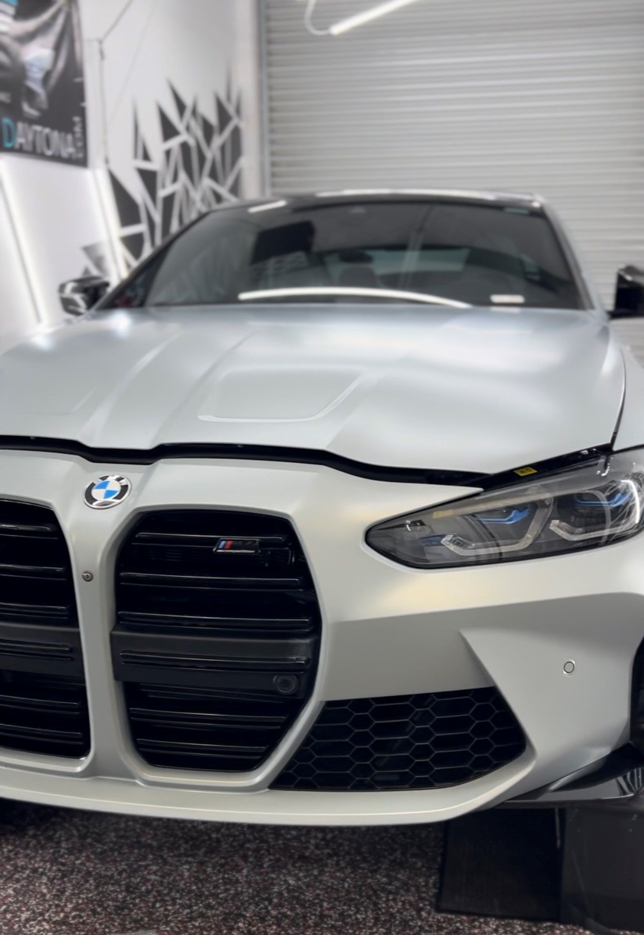 White BMW front view in a garage, with the hood and grille prominently displayed.