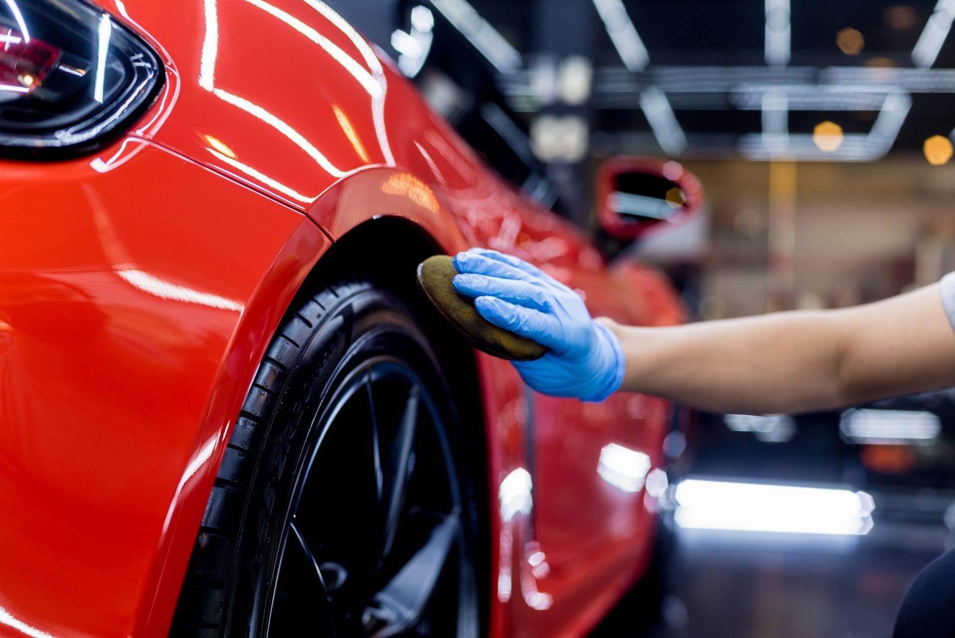 Gloved hand polishing a red car’s rear wheel in an auto shop