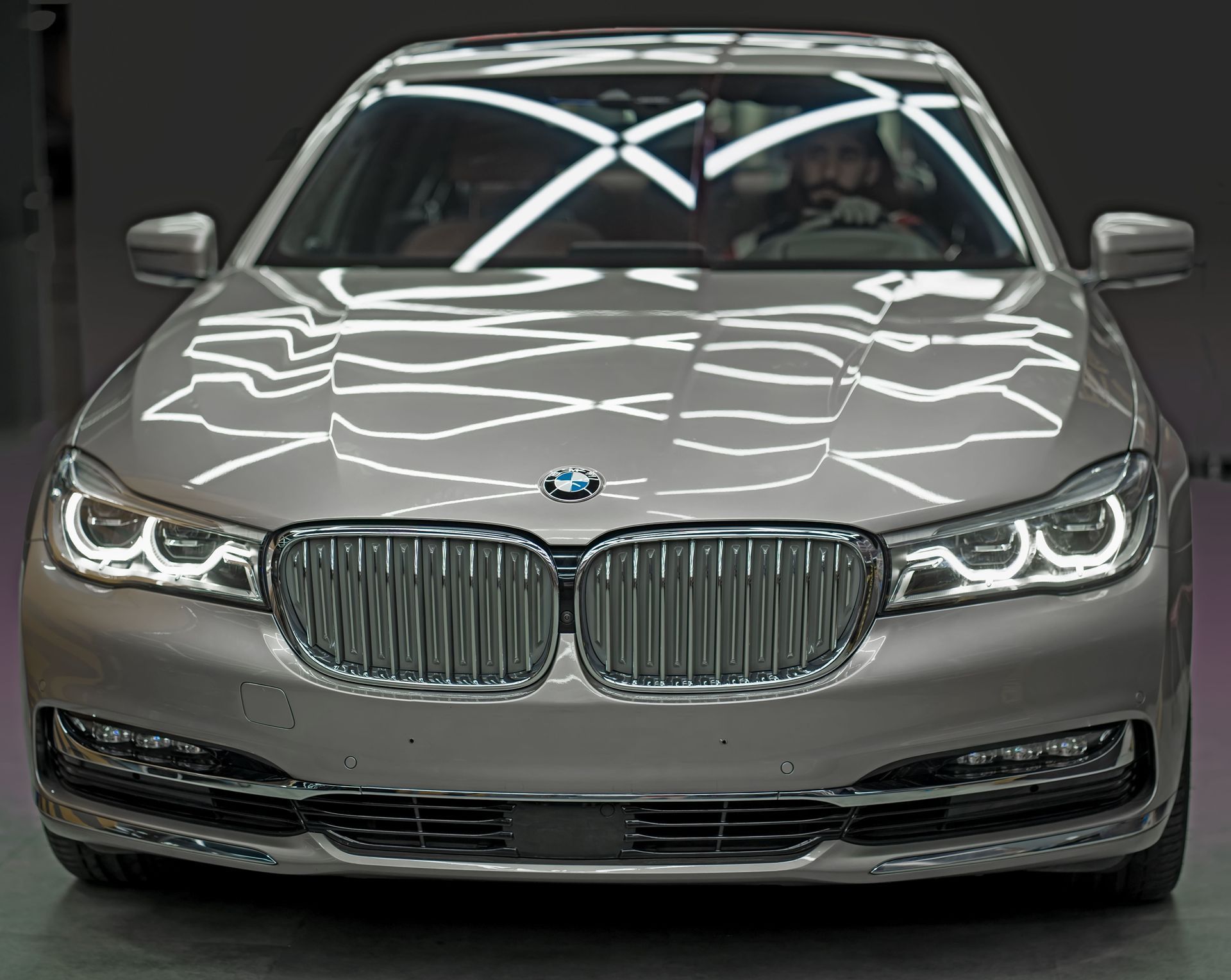 Front view of a silver BMW sedan with headlights on in a dark studio setting