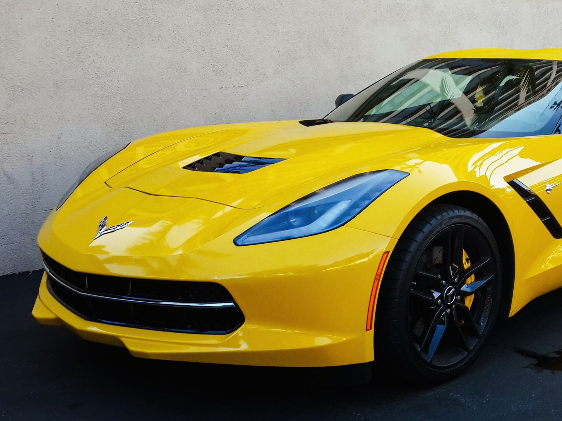 Yellow sports car parked against a gray wall, front view.