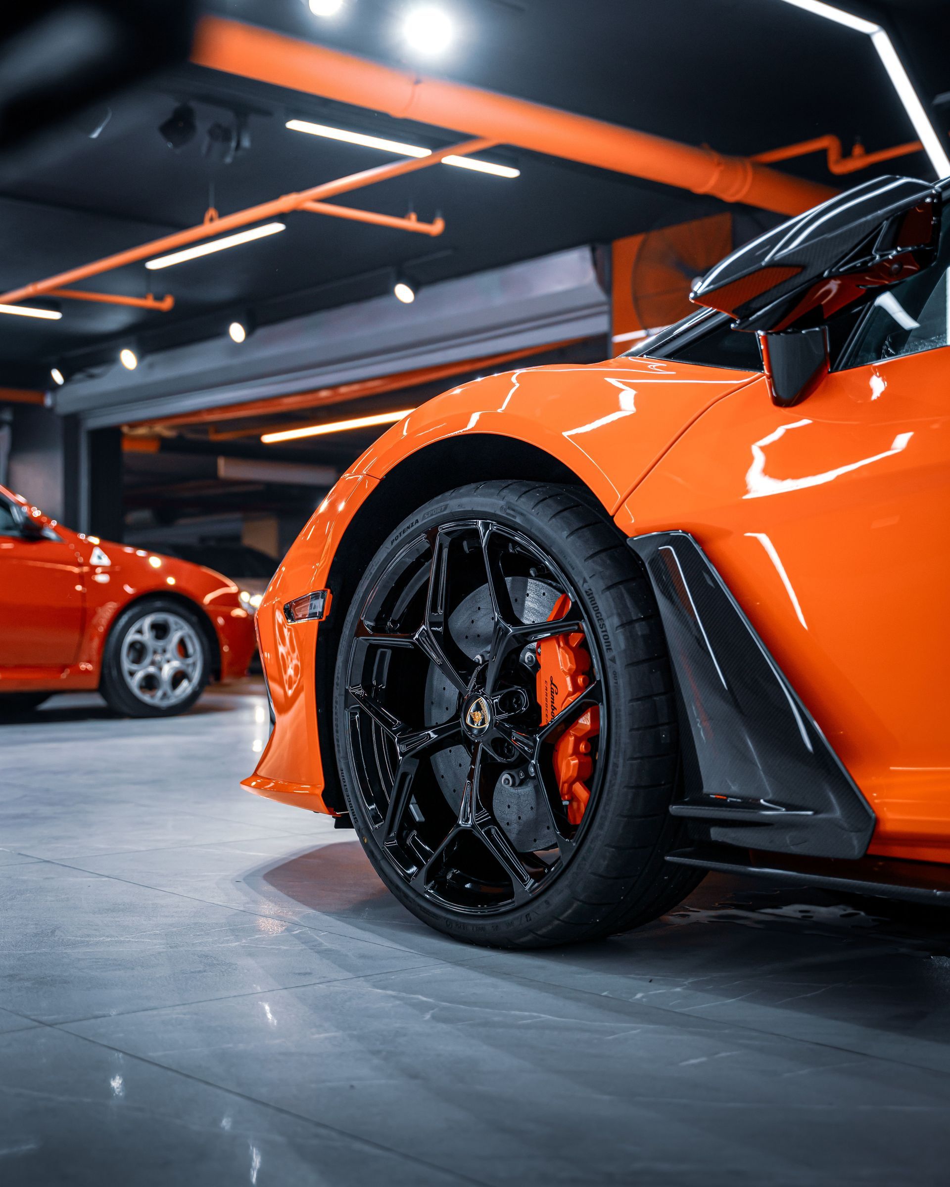 Bright orange sports car in a garage, close-up of black wheel and aerodynamic body kit