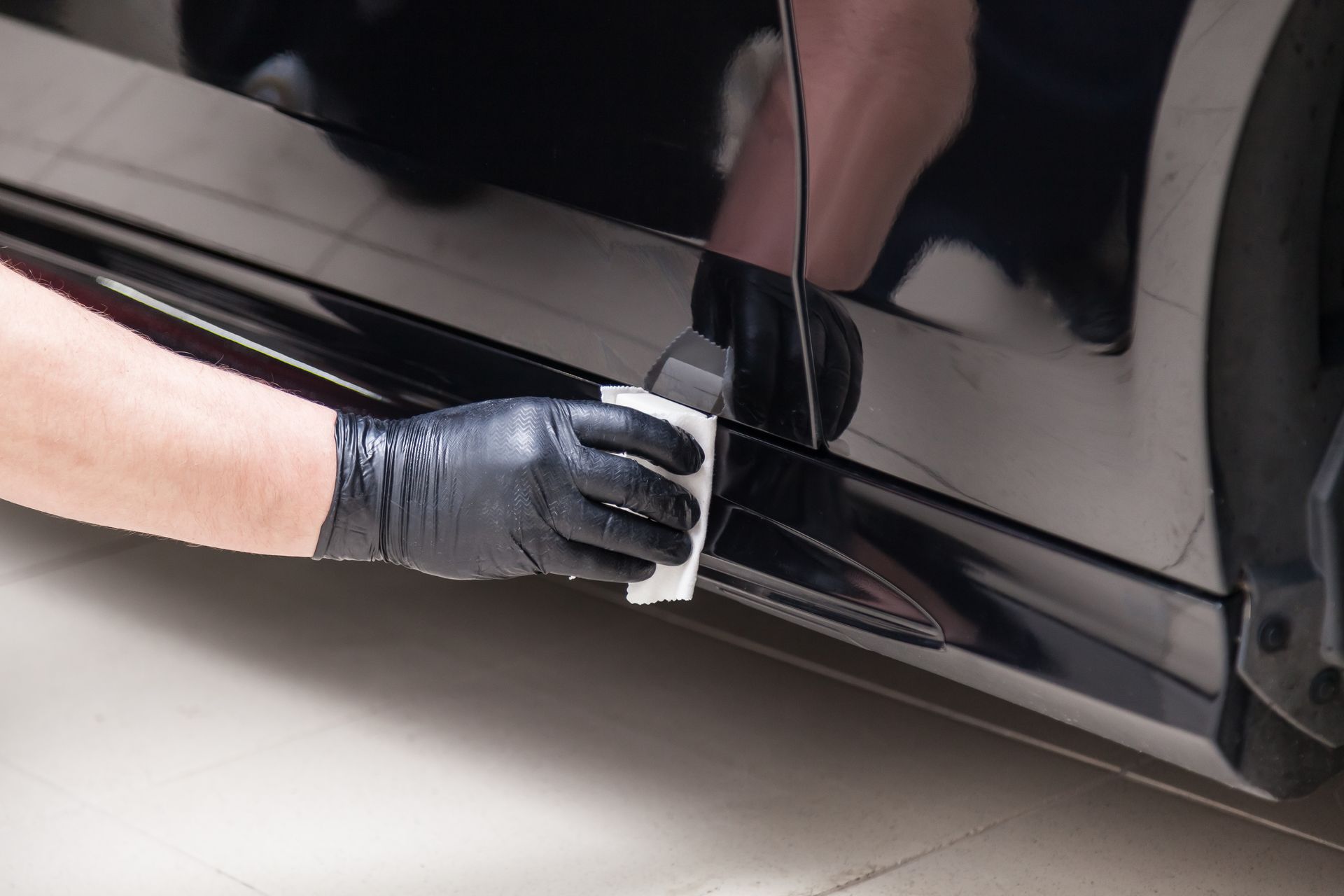 Gloved hand applying protective film to a black car door panel