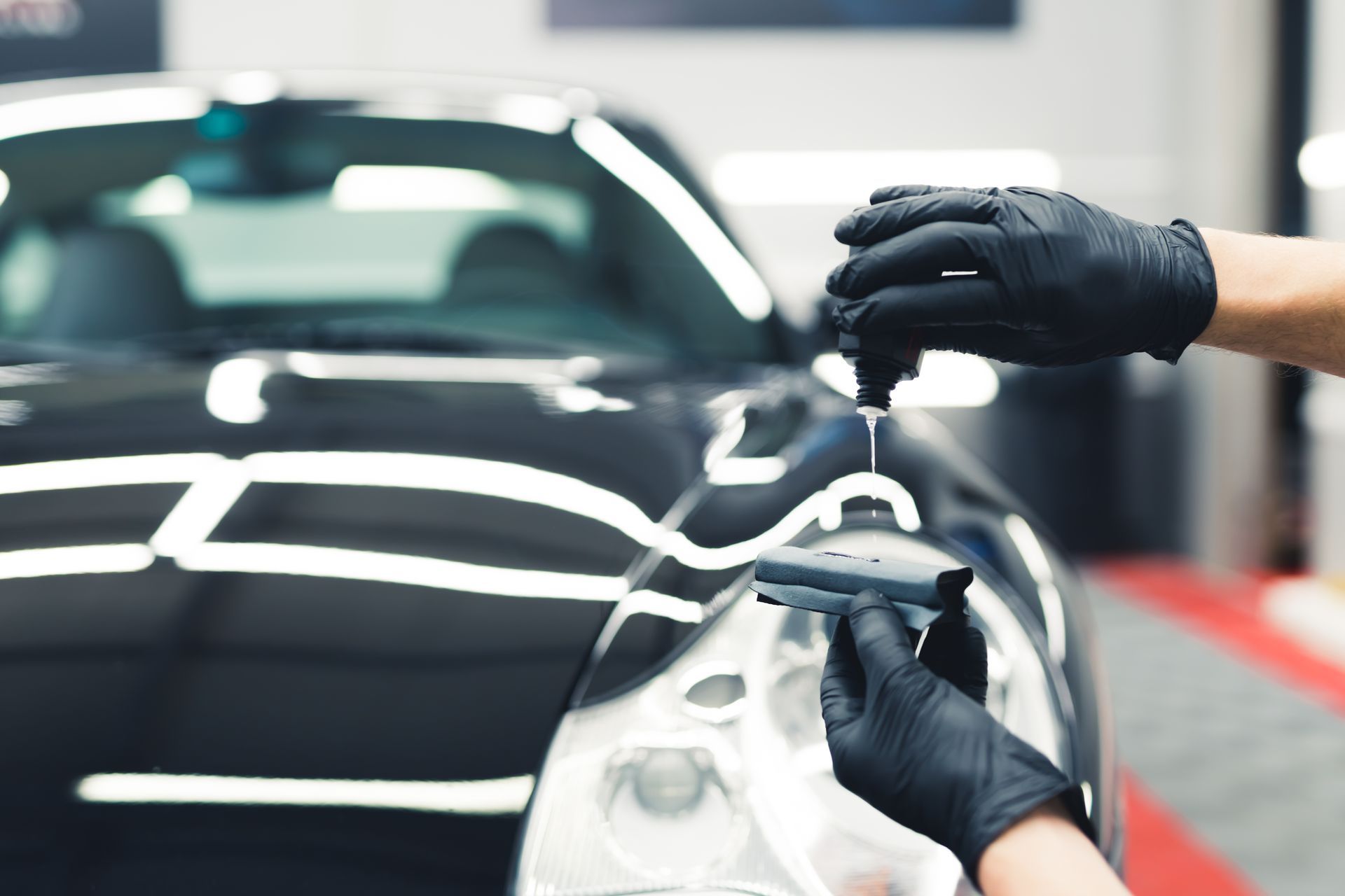 Gloved hands polishing a black car hood with a microfiber cloth in an auto shop