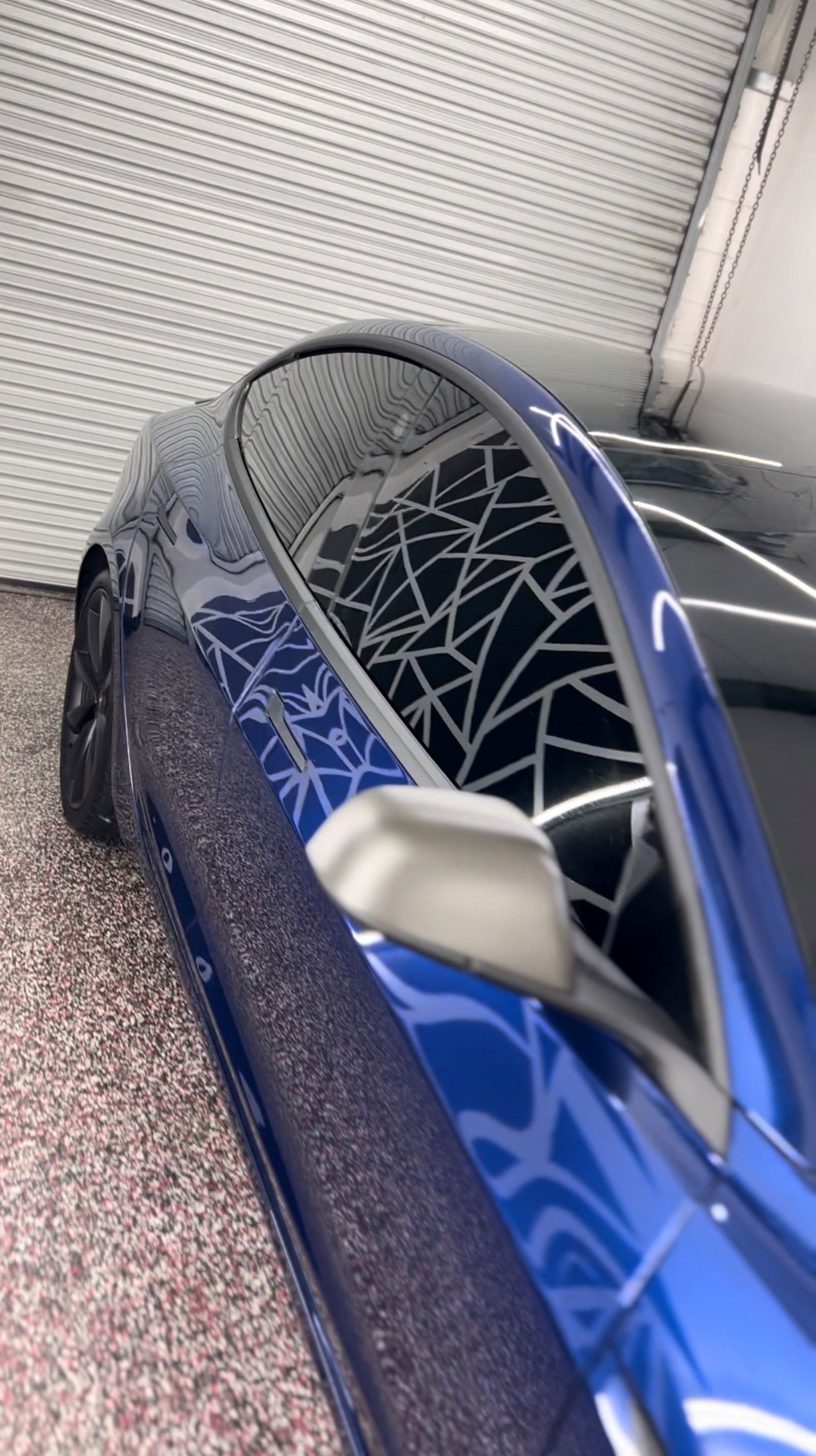 Blue Tesla car with a unique spiderweb design on the window, indoors.