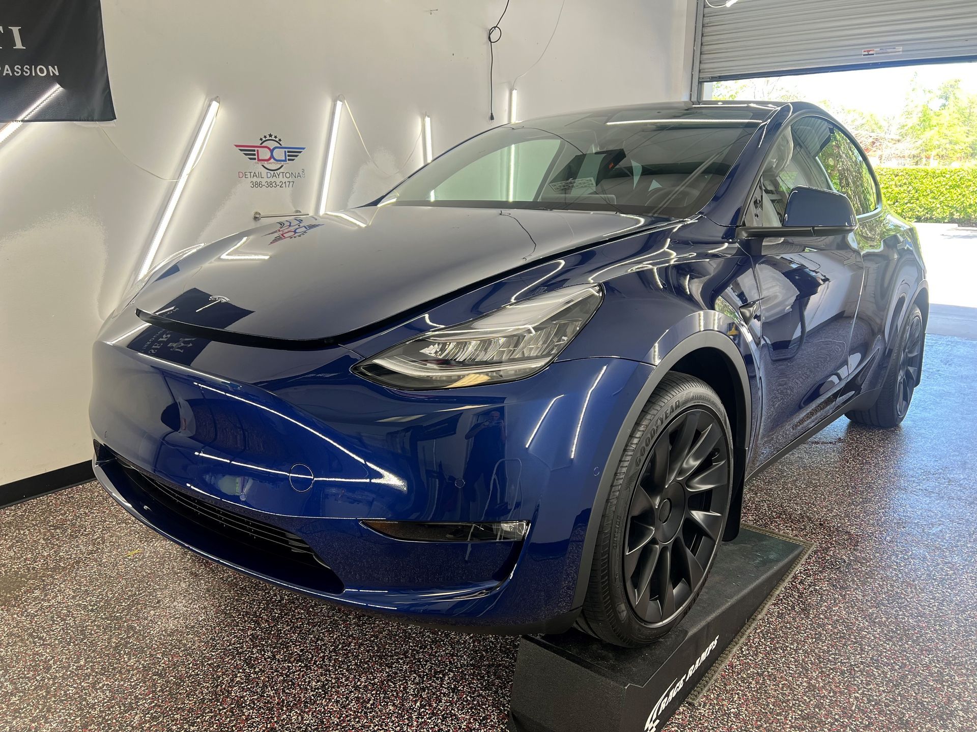 Blue Tesla Model Y, parked in a garage, with black rims.