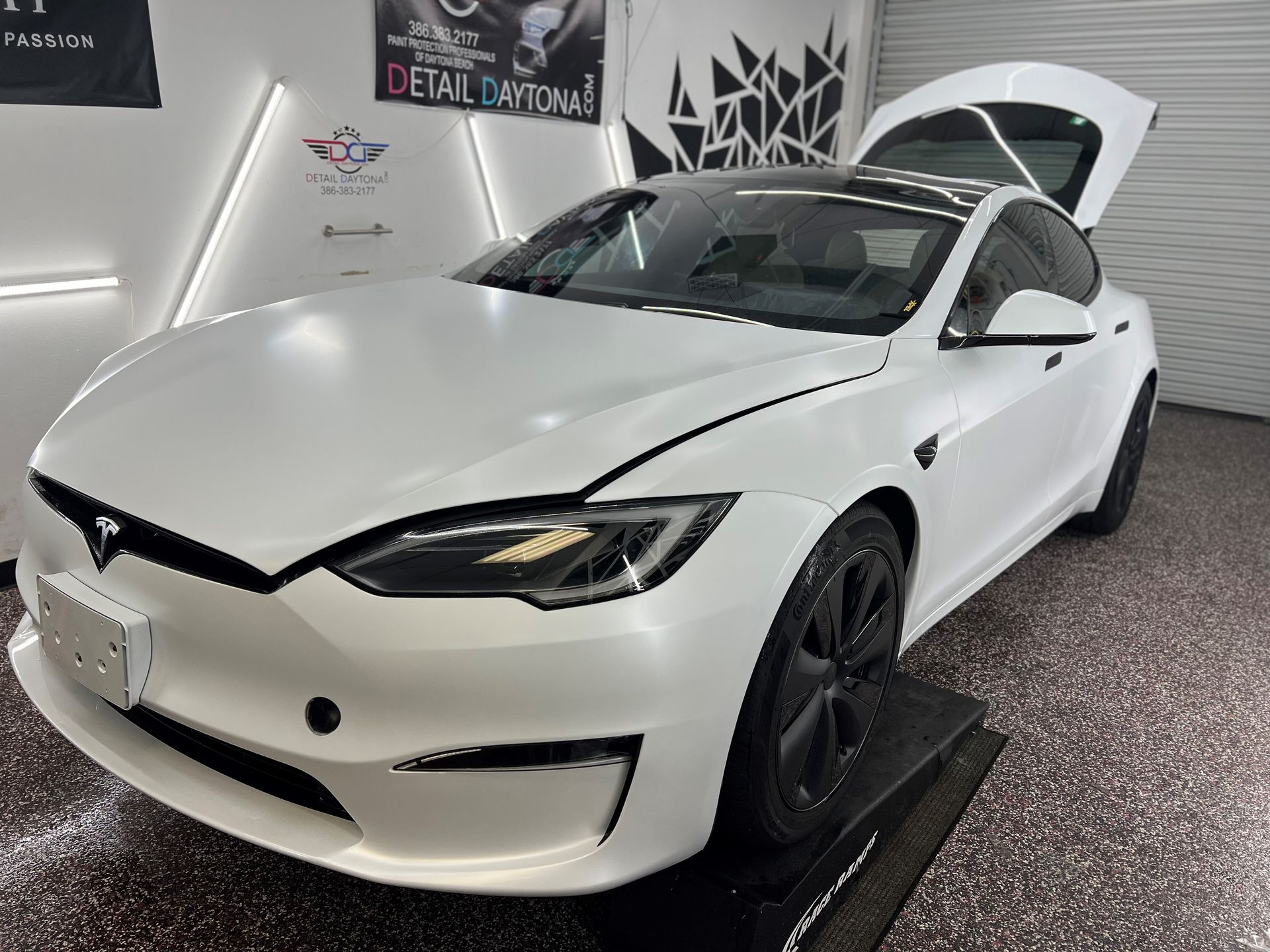 White Tesla with black wheels, trunk open, indoors.
