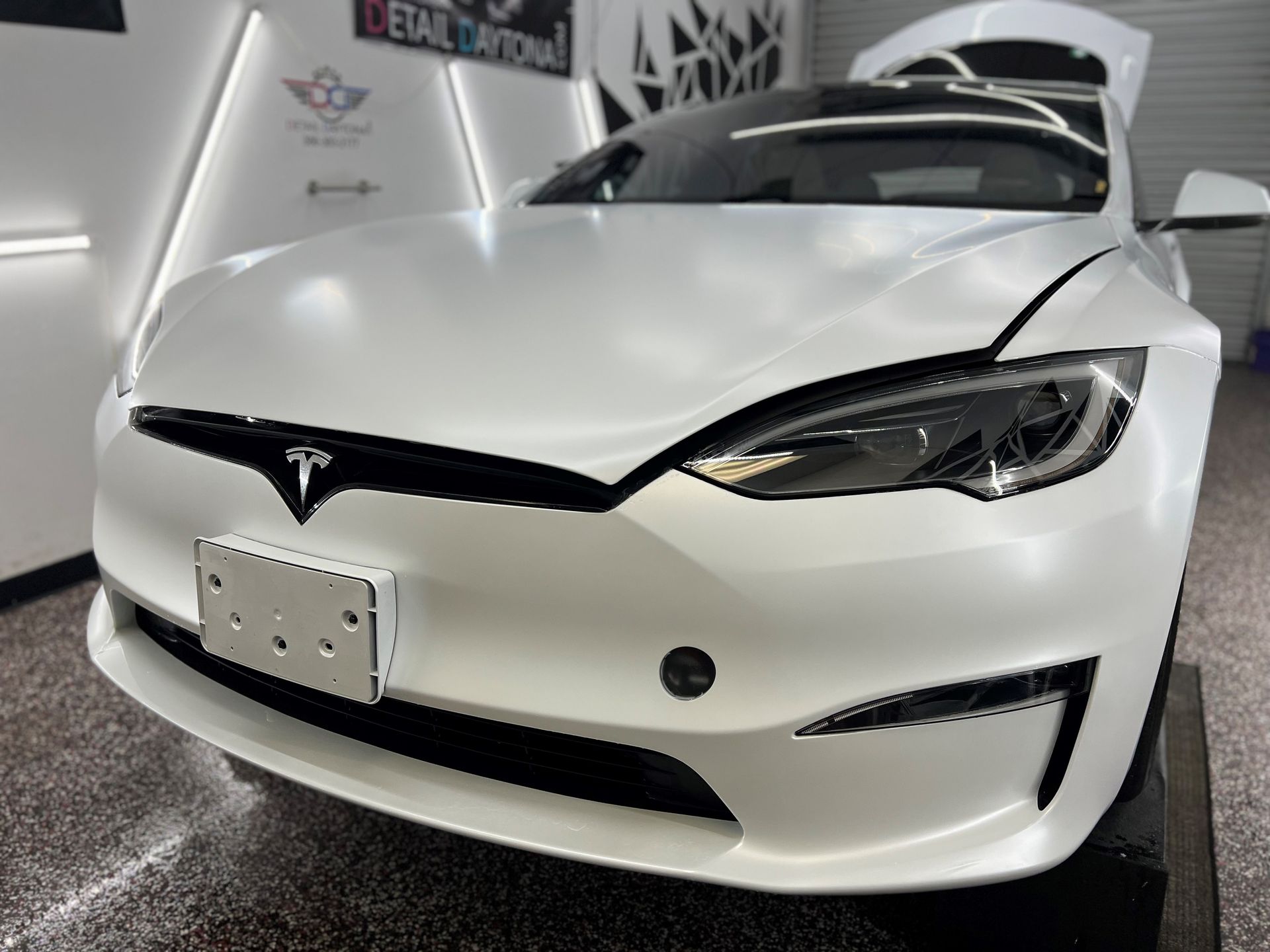 White Tesla with hood and doors open inside a detailing shop.