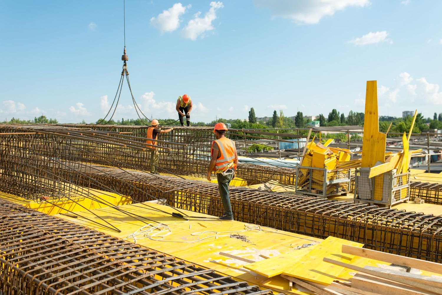Construction workers on a rebar foundation at a bridge site, with yellow machinery and steel framework.