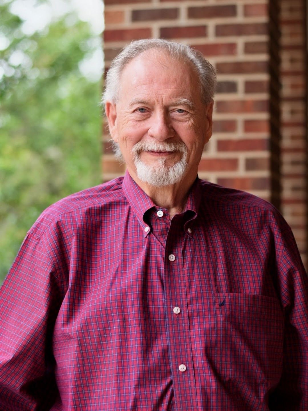 Man seated at a desk in an office, wearing a navy polo and smiling in front of bookshelves.
