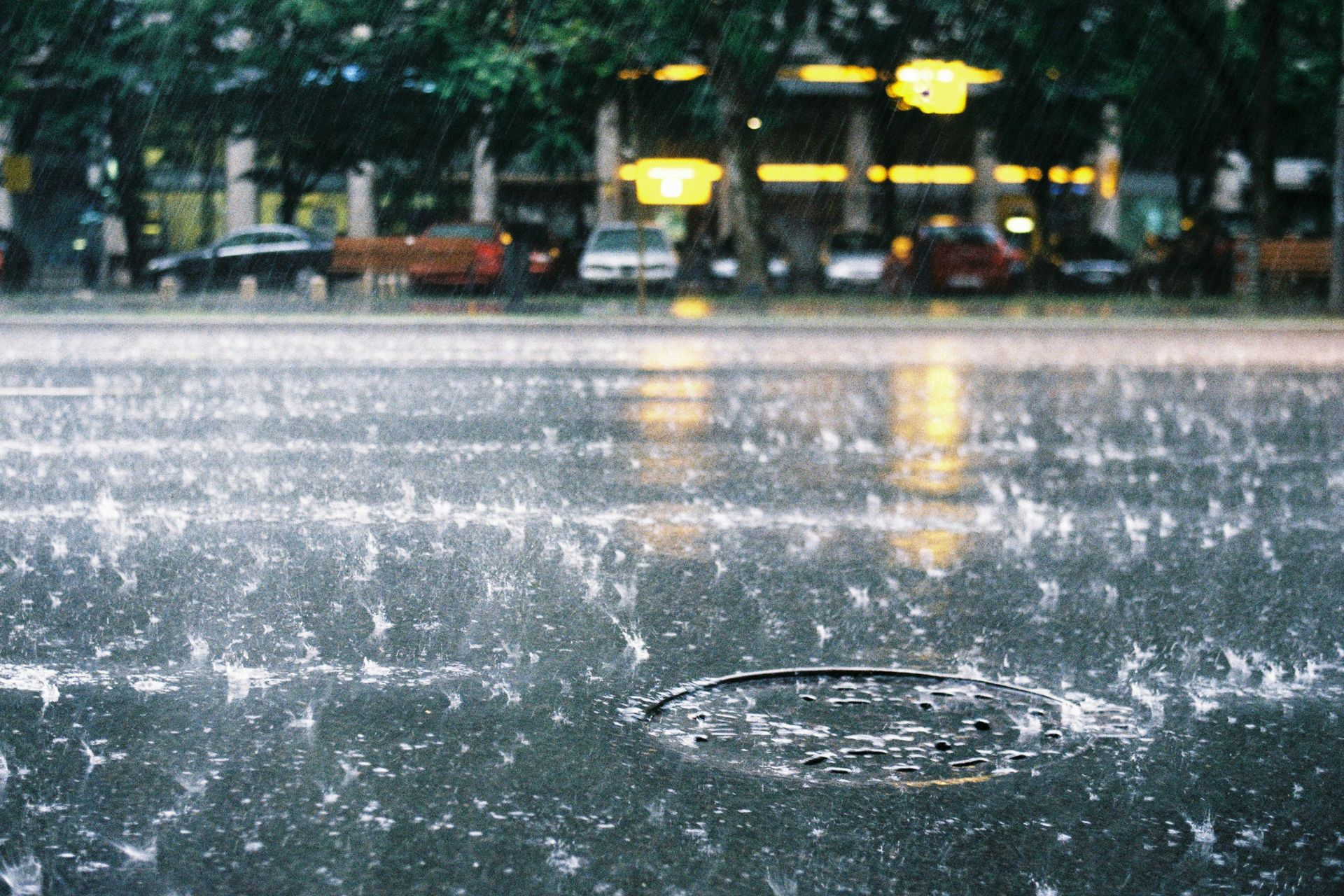 Rain splashing on a wet street with blurred yellow buses in the background