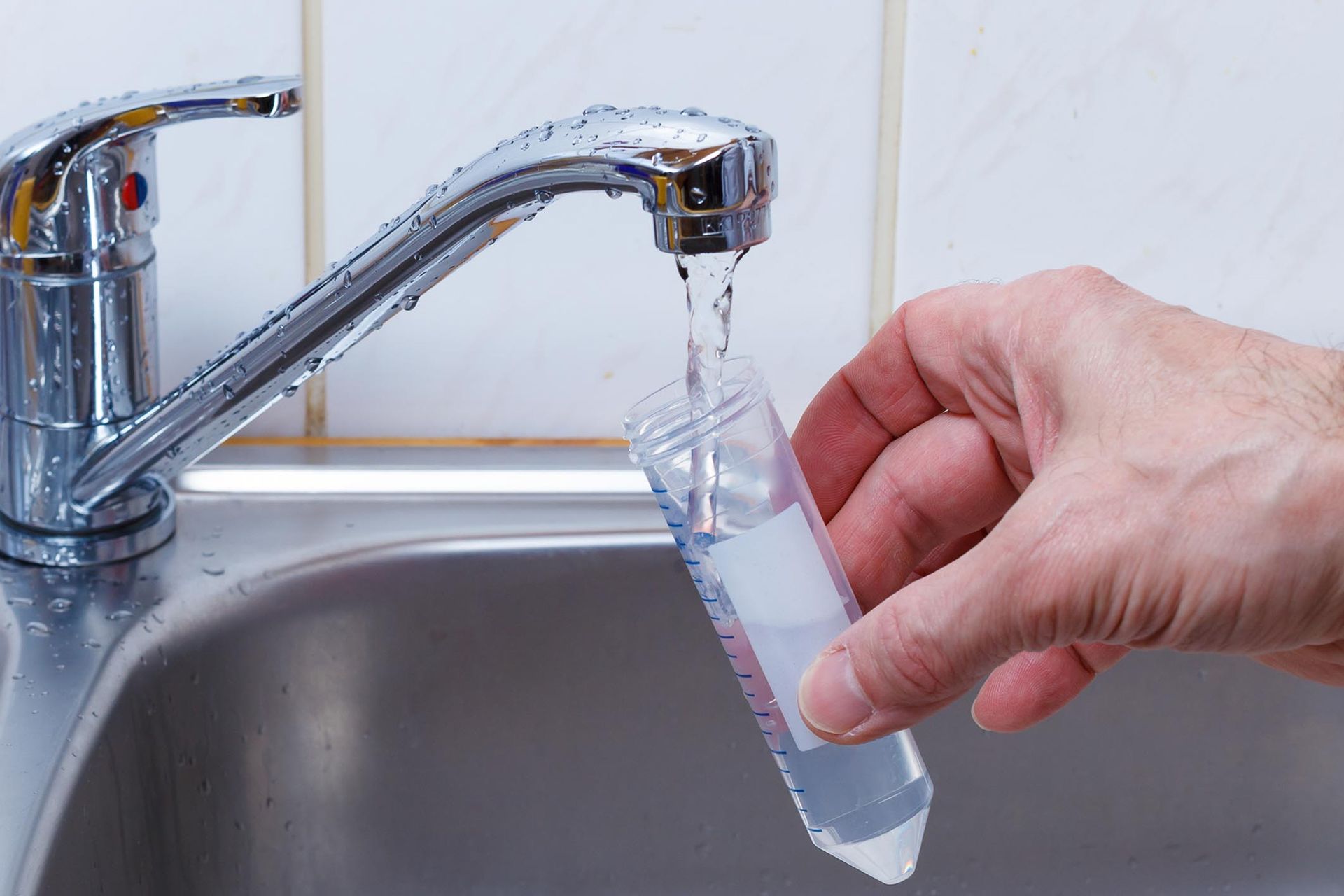A person is pouring water into a measuring cup in a sink