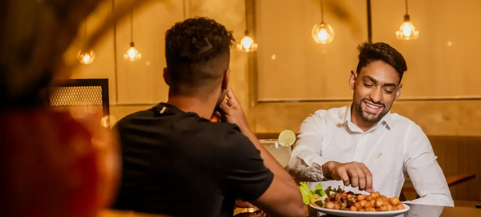 Duas pessoas jantando em um restaurante com iluminação aconchegante, uma servindo a refeição e sorrindo.