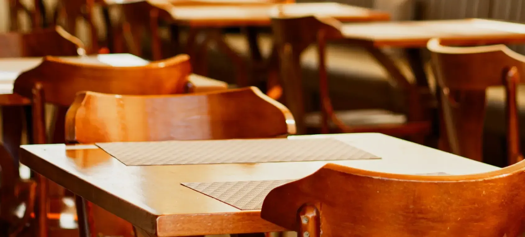 Mesas e cadeiras de madeira vazias em uma sala de aula ou auditório com iluminação aconchegante.