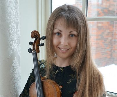A woman is holding a violin in front of a window.