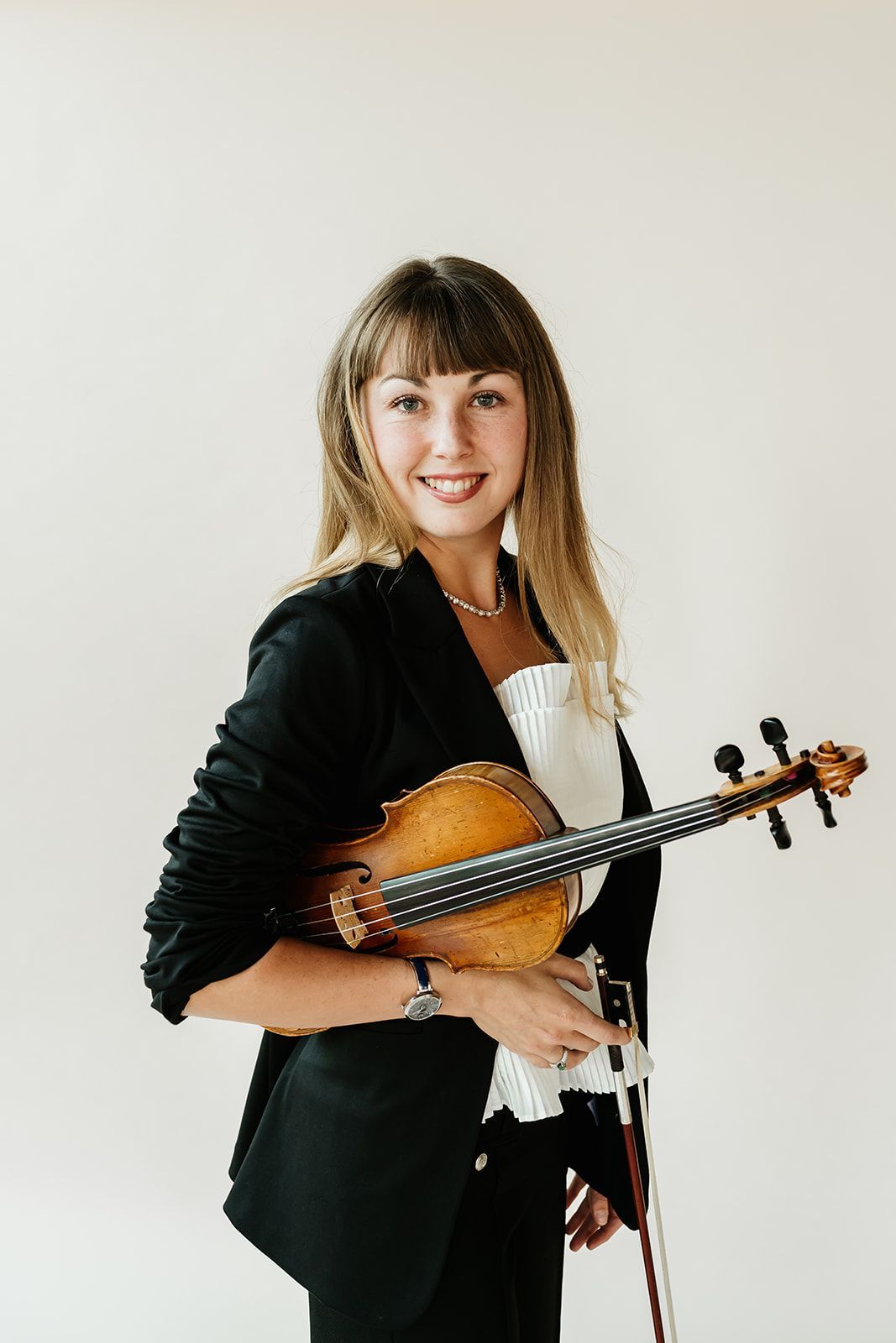 A woman in a white tank top is holding a violin and smiling.
