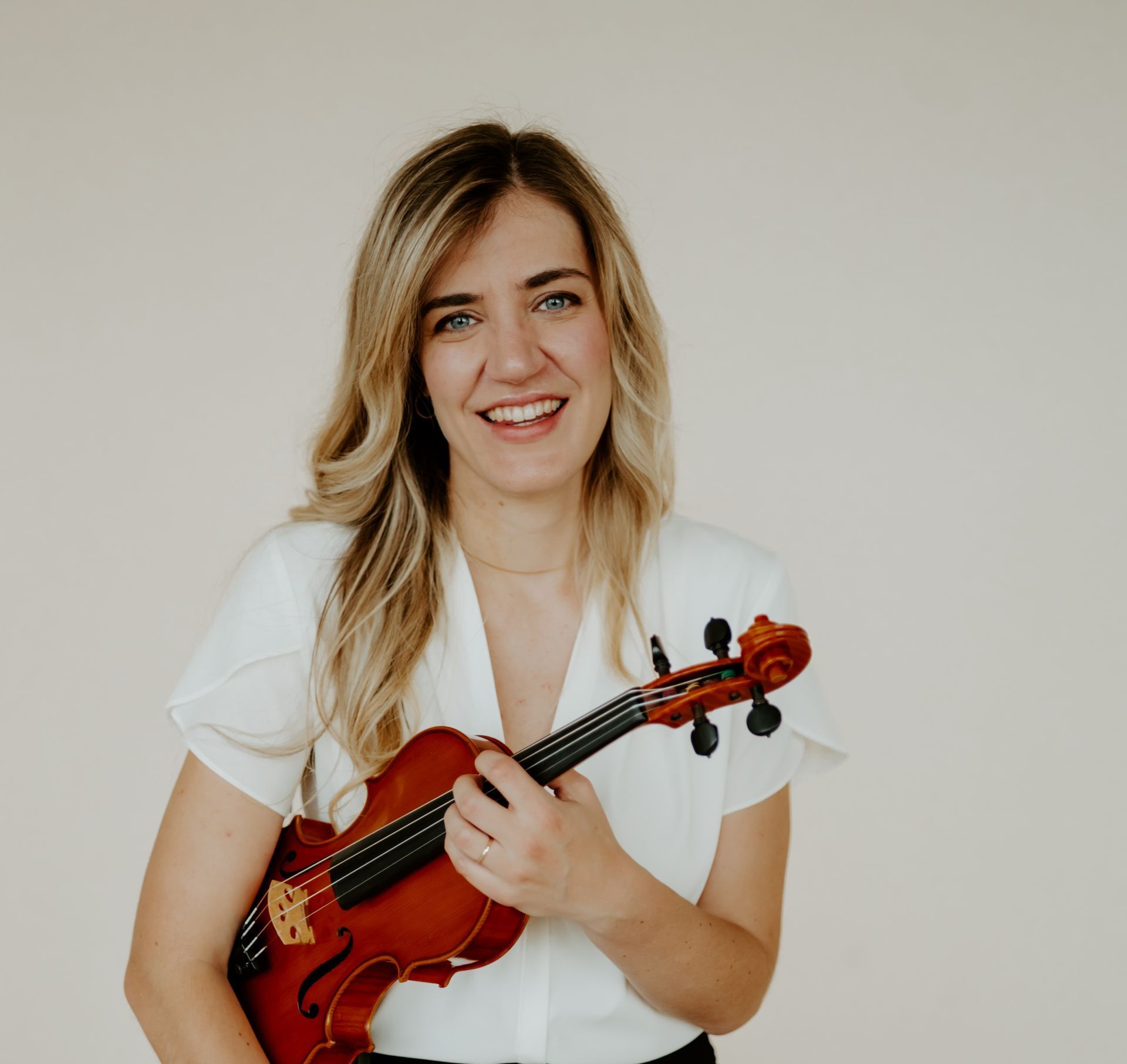 A woman in a white shirt is holding a violin and smiling.