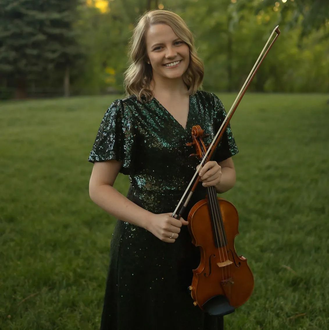 A woman is holding a violin in front of a window.