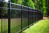 A black metal fence stretches across a green lawn in front of trees.