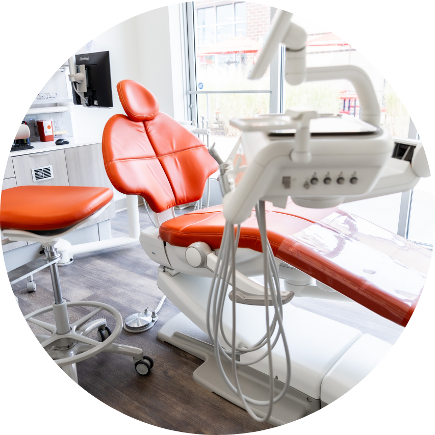 Orange dental chair in a dentist's office with medical equipment and bright window in the background.