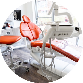 Orange dental chair in a bright dental office; medical equipment and window in background.